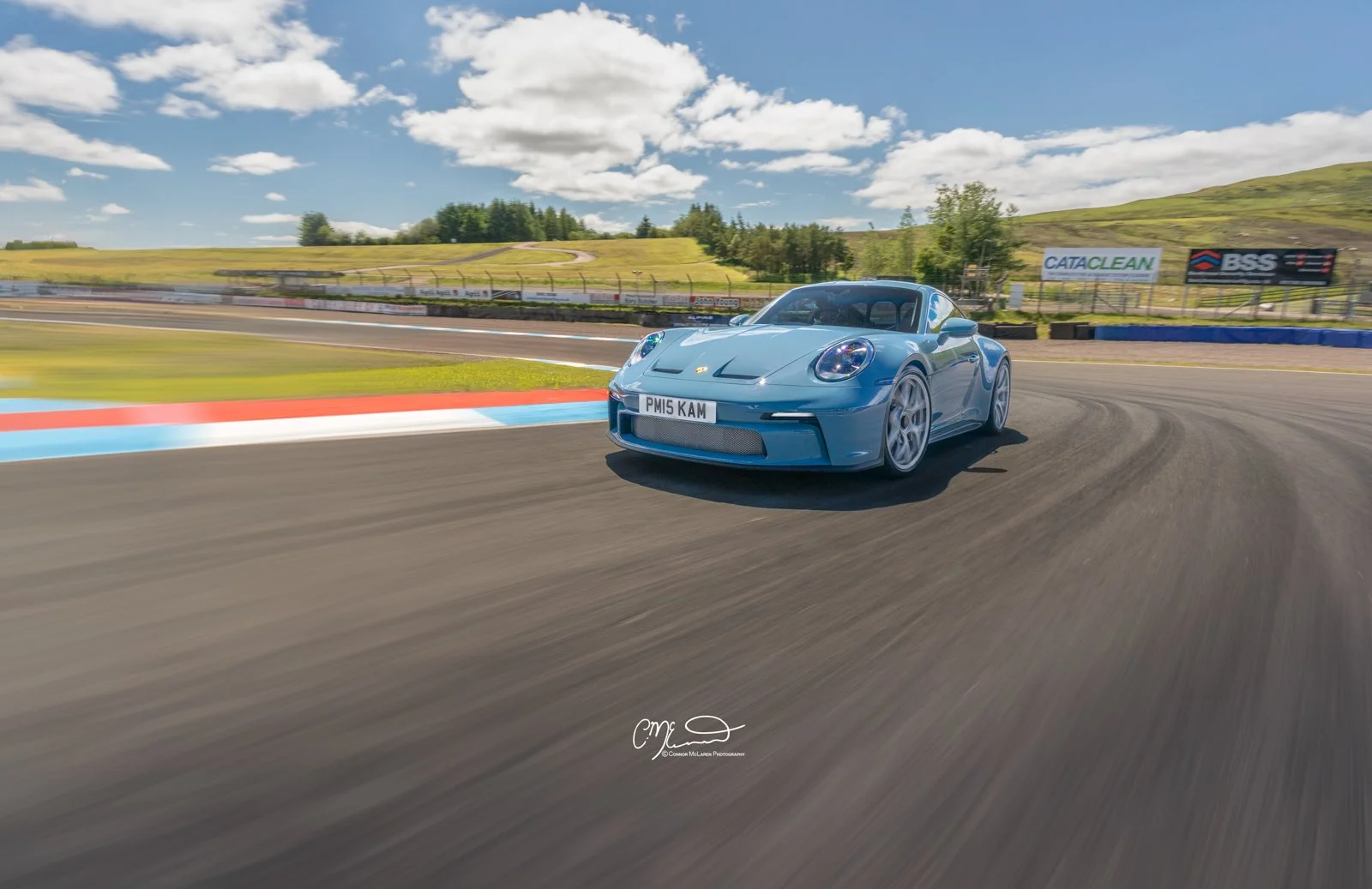 Porsche 911 ST on track at Knockhill. Blue sports car racing on a track with green hills and blue sky in the background.