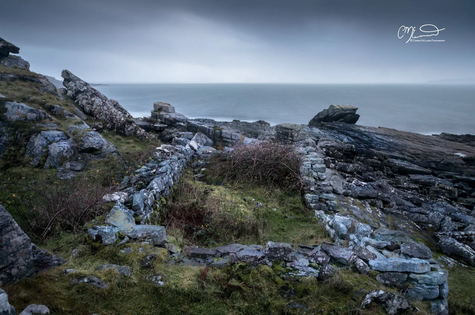 Scotland, Isle of Skye, Elgol. Coastal scene with rocky shoreline, weathered stones, and an ocean in the background on a cloudy day.