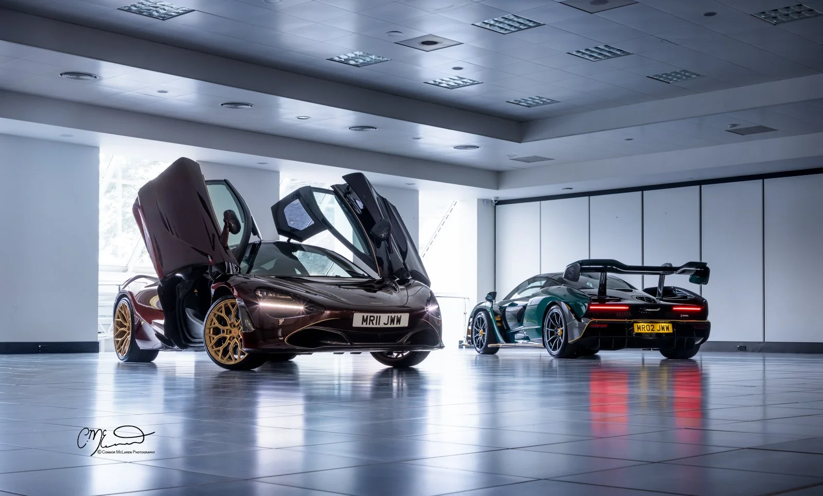 Mr JWW McLaren Senna MSO full carbon. Two luxury sports cars in a showroom, one with gullwing doors open and the other with a large rear wing, both featuring sleek black and green exteriors.
