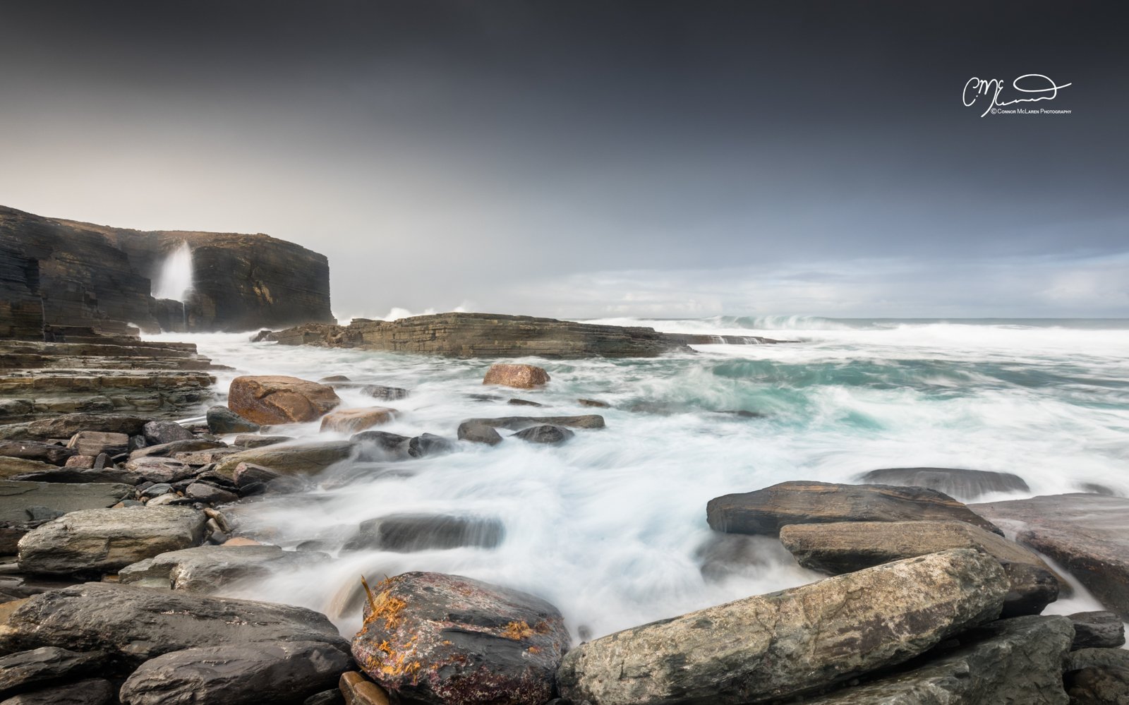 Skara Brae, Orkney, Scotland. Coastal scene with rocky shoreline, crashing waves, and overcast sky.