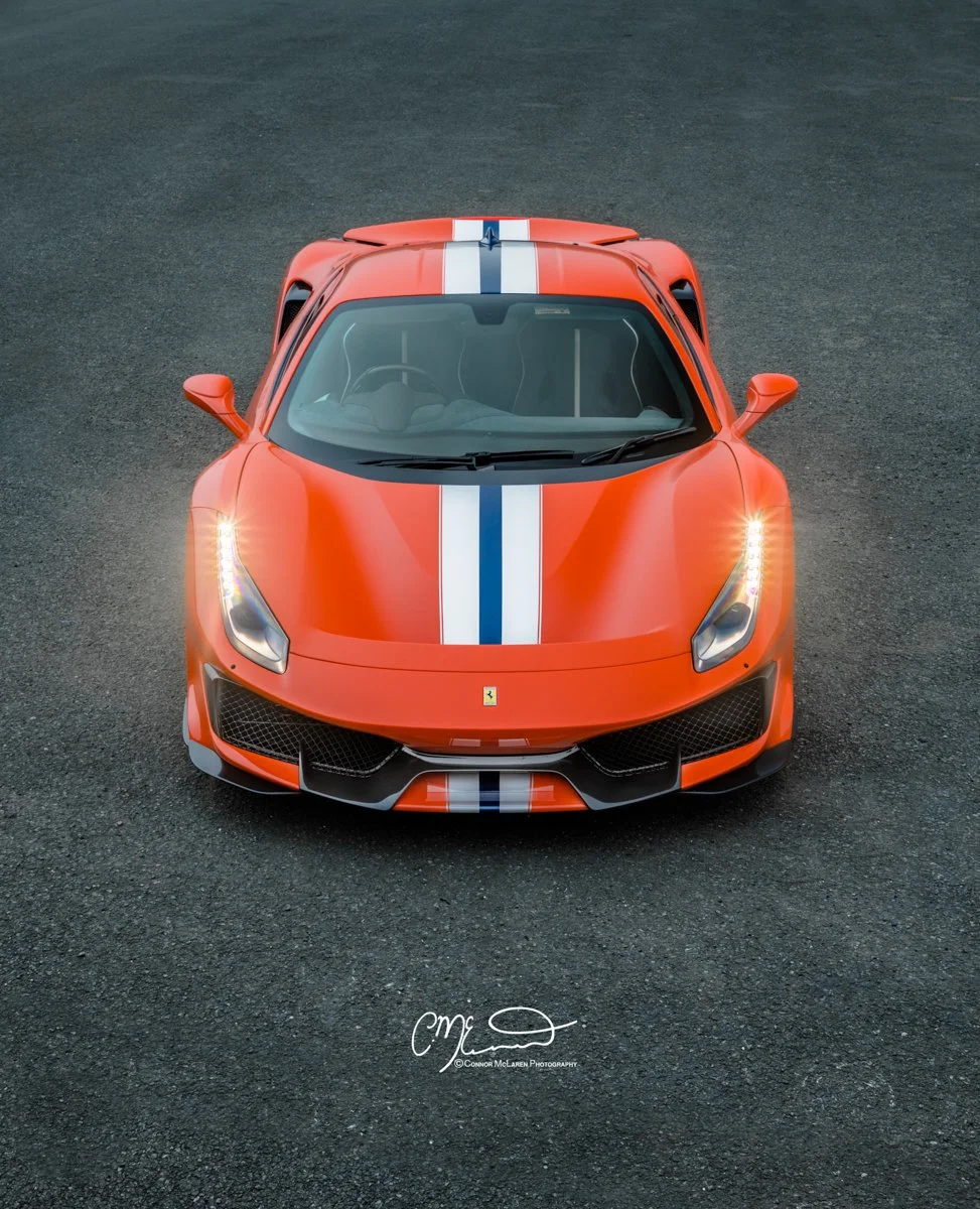 Ferrari 488 Pista. Front view of a red Ferrari sports car with white and blue racing stripes on a dark asphalt surface.
