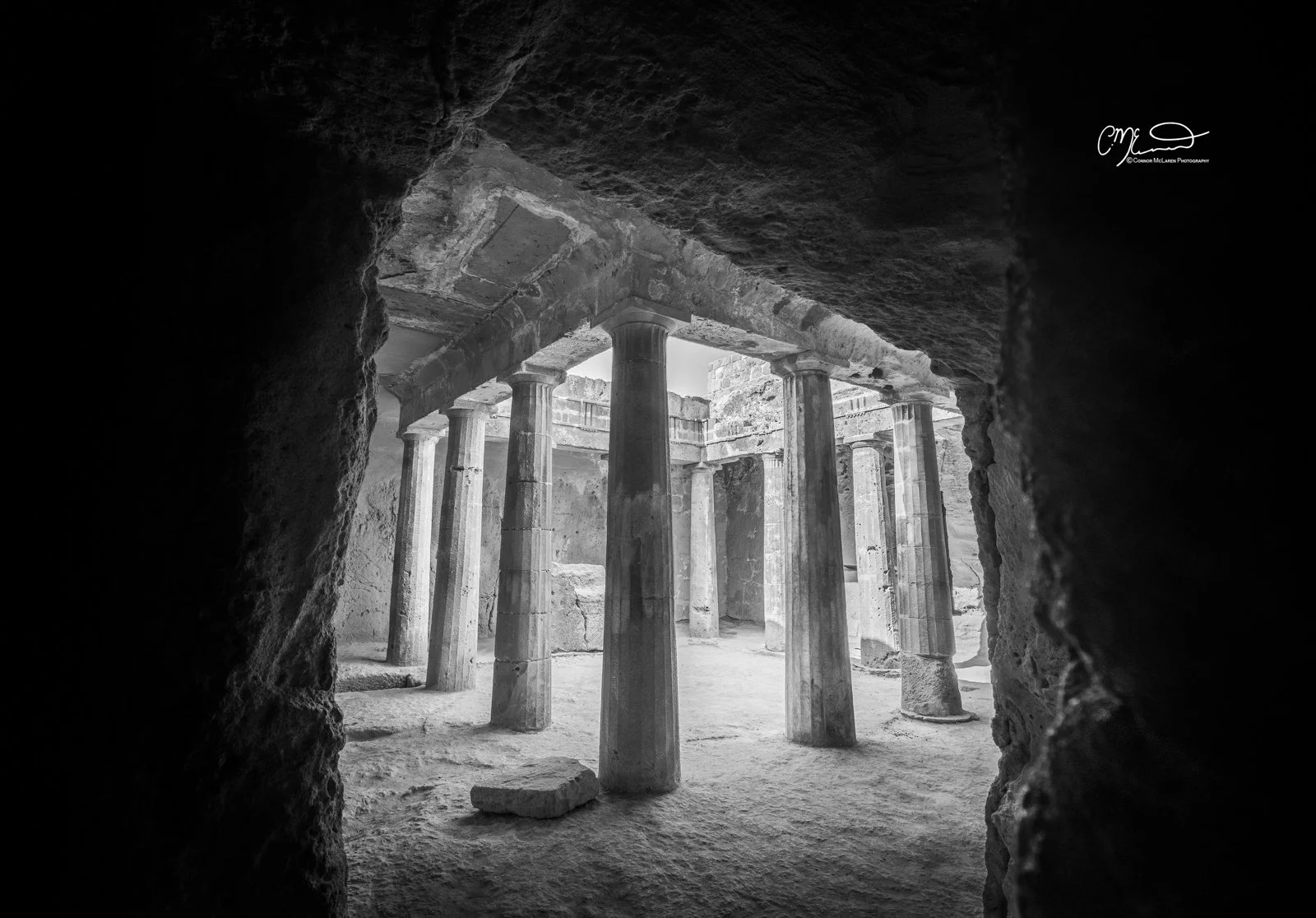 Cyprus. Black and white photo of ancient stone ruins with columns seen through a rough stone opening.