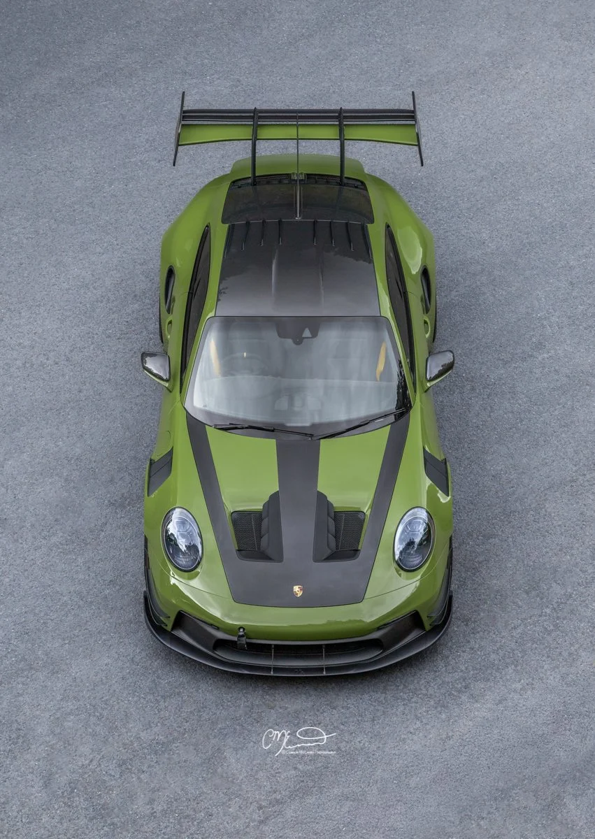 Porsche 911 GT3 RS in Paint to sample Olive green with full Manthey Racing kit. Top view of a green Porsche race car with black accents, a large rear wing, and a sleek aerodynamic design, parked on a gray asphalt surface.
