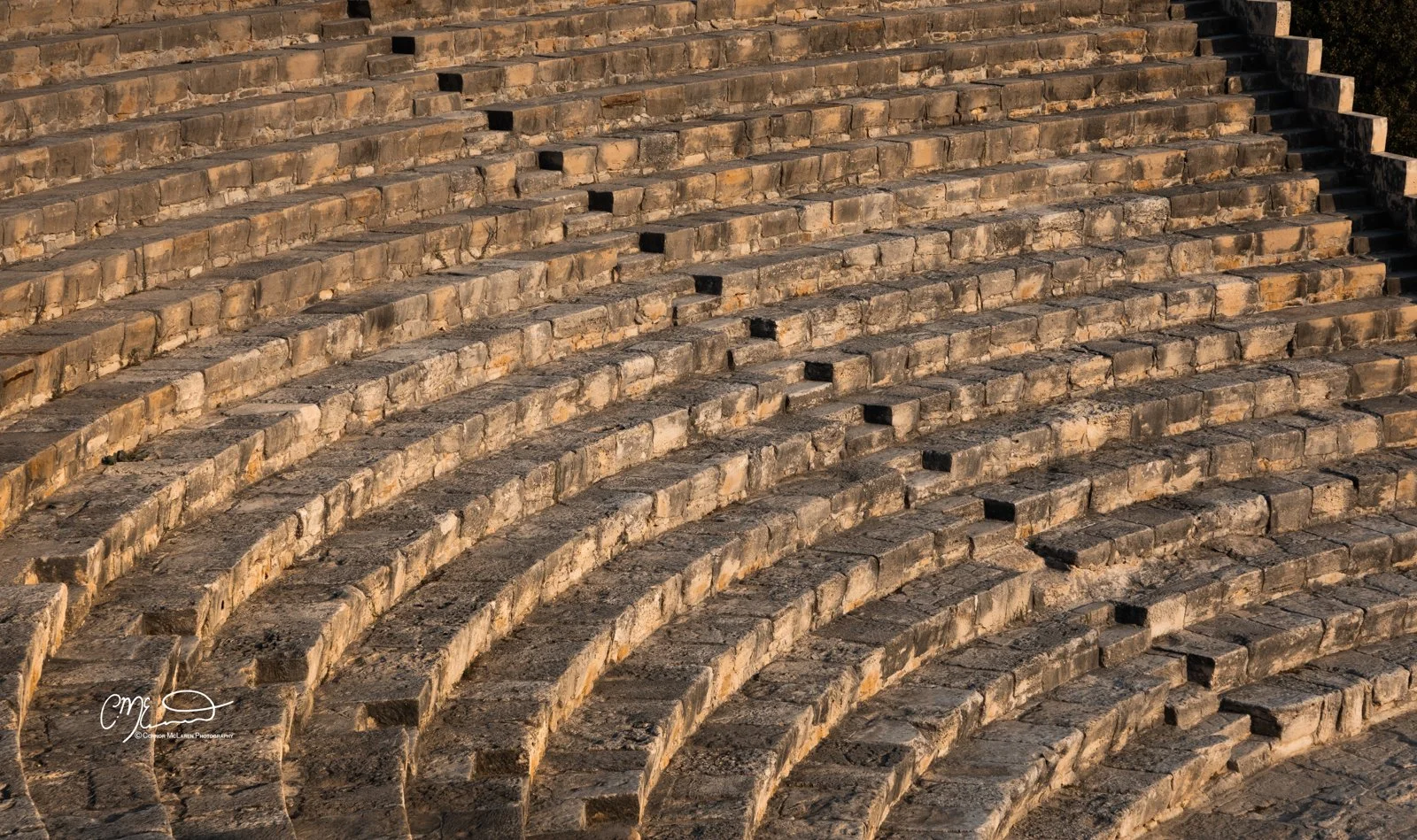 kourion, Cyprus. Close-up view of a large stone amphitheater with curved stone seating steps in sunlight.