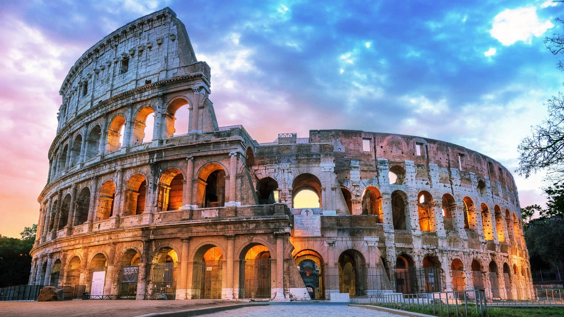 The ancient Roman Colosseum illuminated at sunset with a dramatic sky overhead.