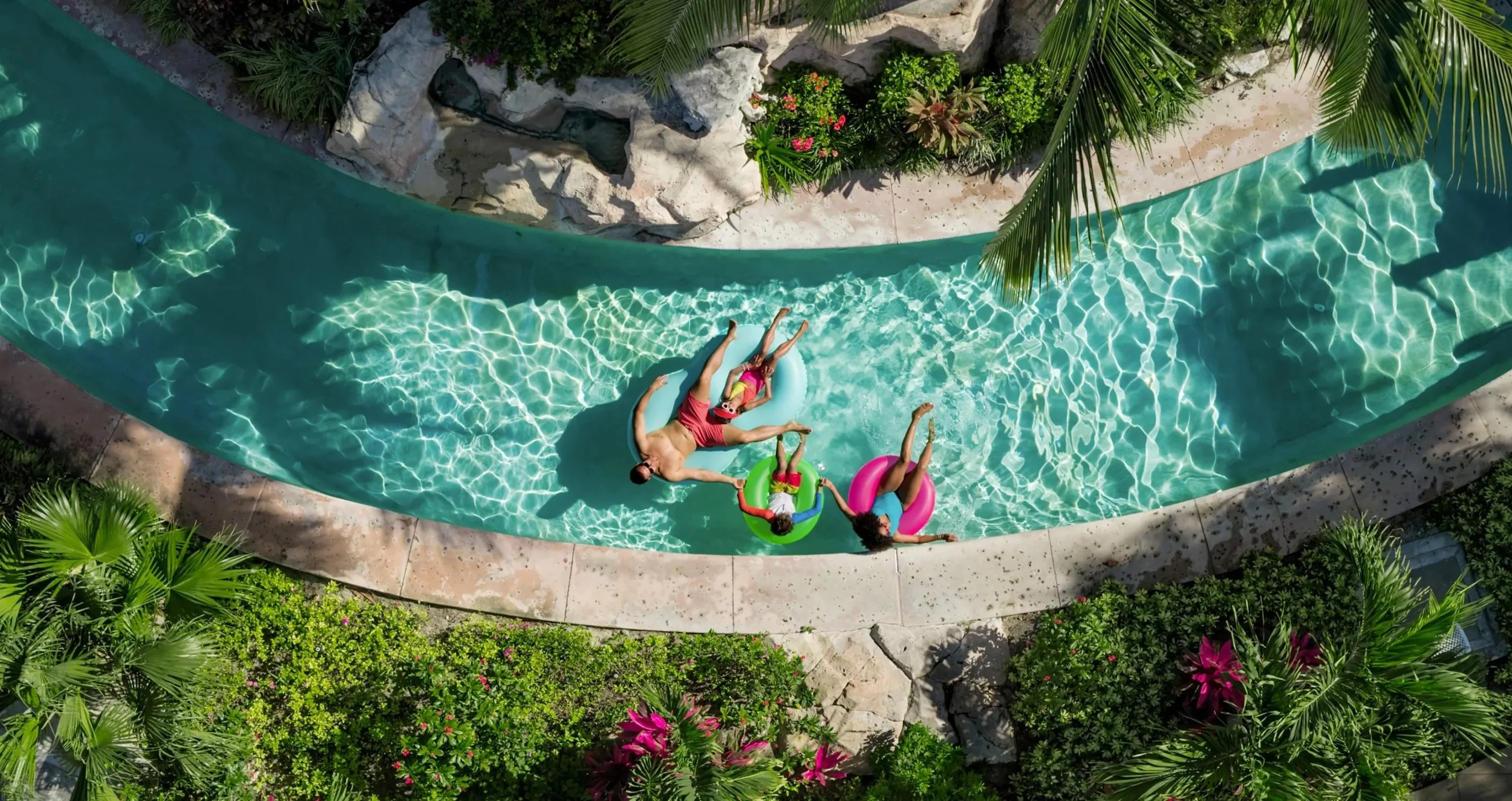 A family enjoying a summer day on a waterslide surrounded by lush tropical plants and flowers