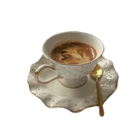 A cup of coffee in a delicate white cup with gold decorations and a gold painted handle.