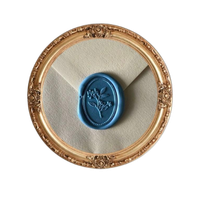 A baby blue wax seal on a white envelope in a circular gold frame.