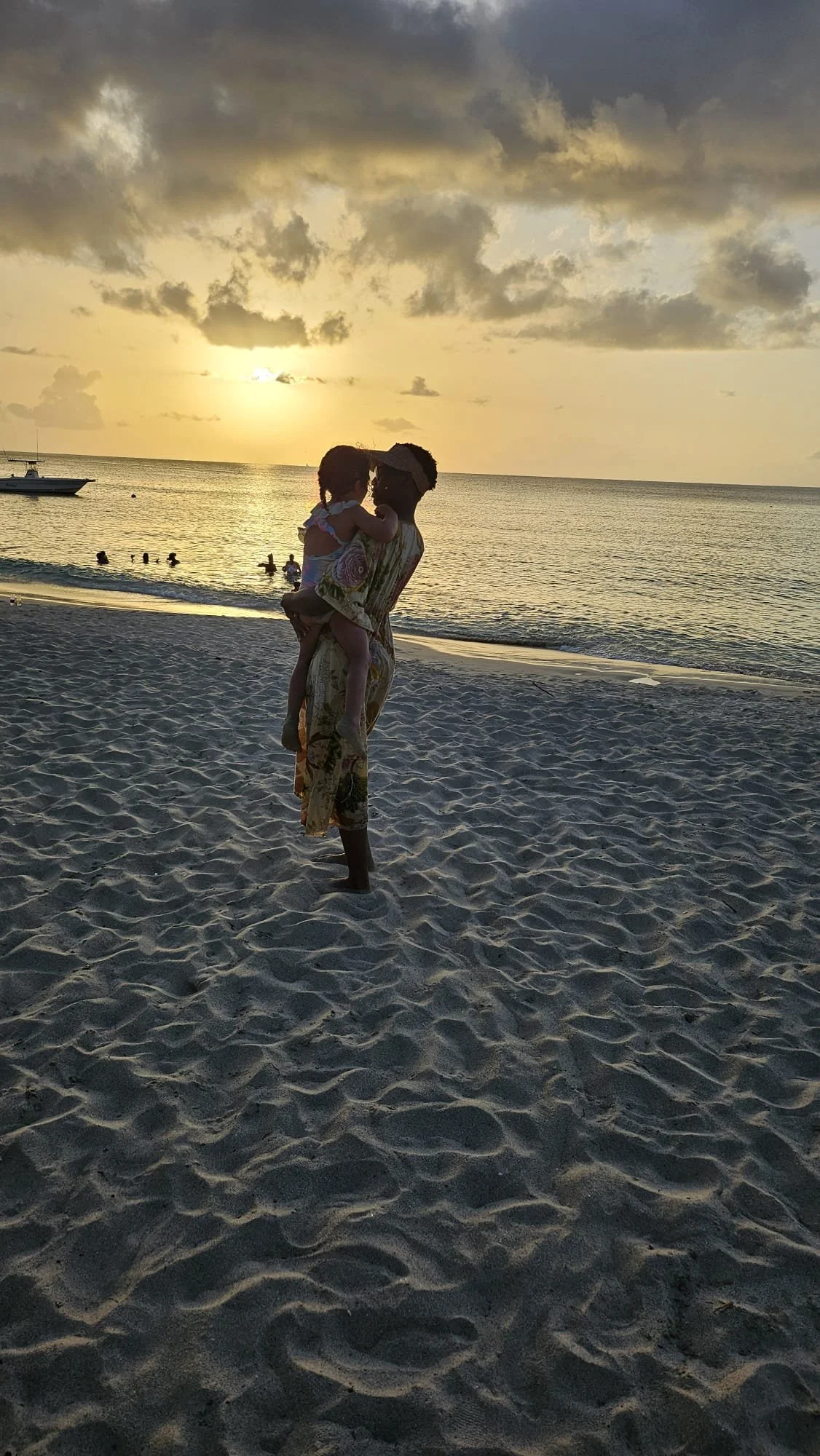Silhouette of a mother holding her child on a sandy beach at sunset, looking out at the ocean, representing family connection and restorative luxury travel.