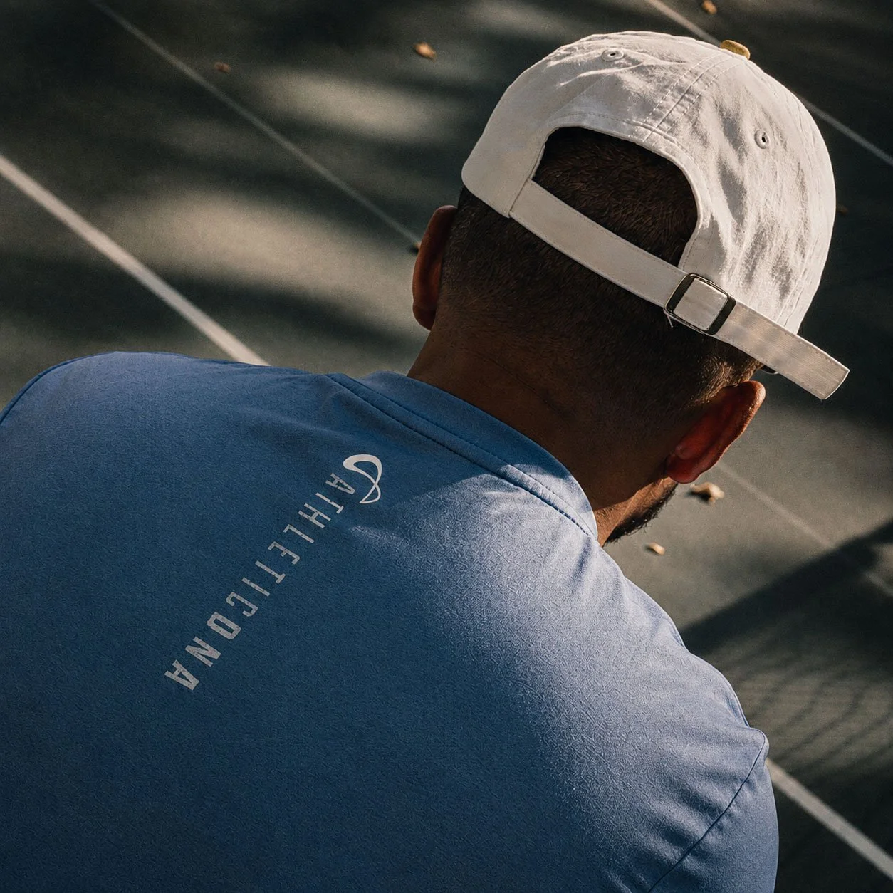A person wearing a white baseball cap and a blue shirt with 'GOLFETI' on the back, sitting on a golf course, viewed from behind.