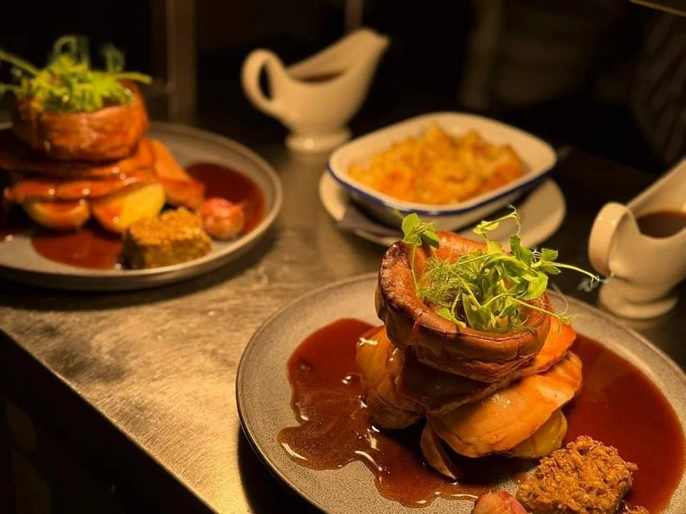 Plates featuring roast dinners with Yorkshire puddings, meat, roasted vegetables, gravy, and garnish.