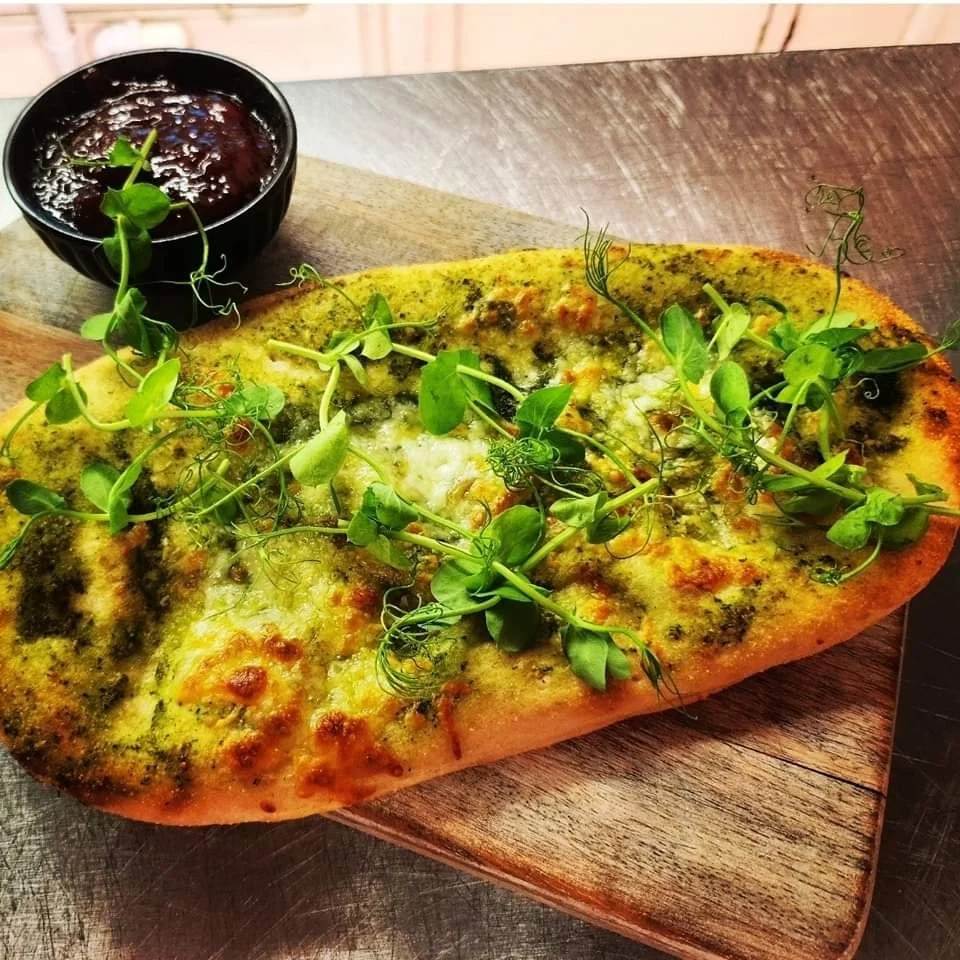 Flatbread with greens on a wooden board.