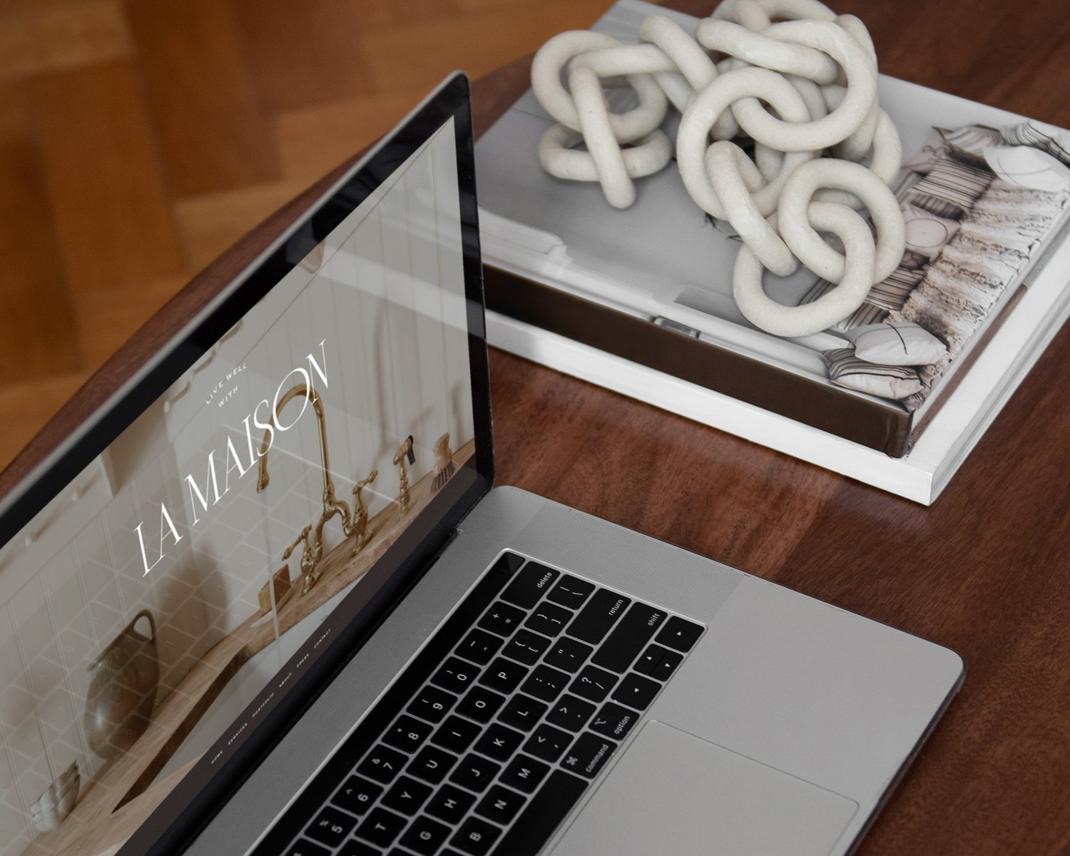 a laptop showing an interior designer's squarespace site on a wood coffee table next to a stack of books