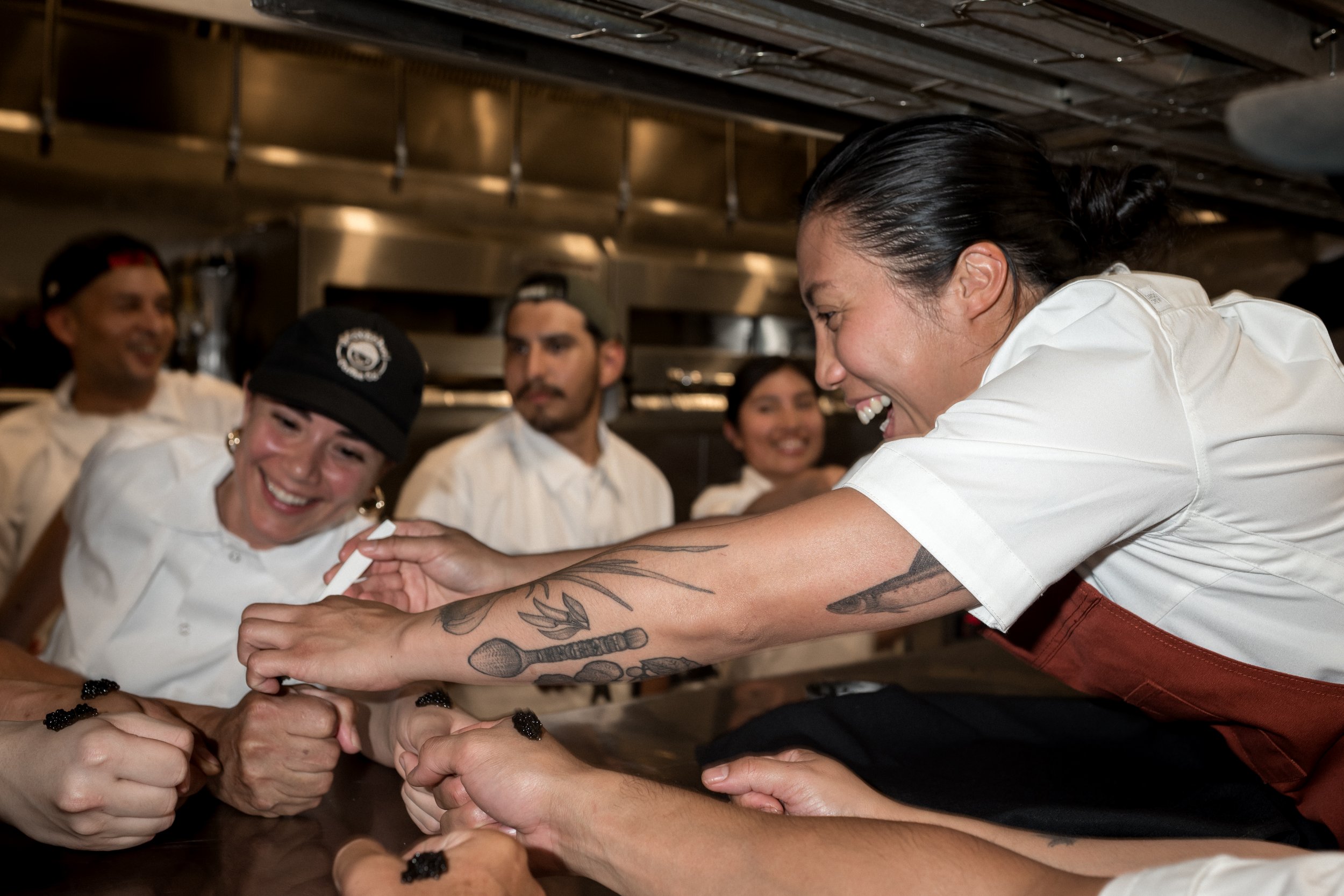 Chef Tara Monsod in the kitchen with her team smiling about to take a caviar bump.