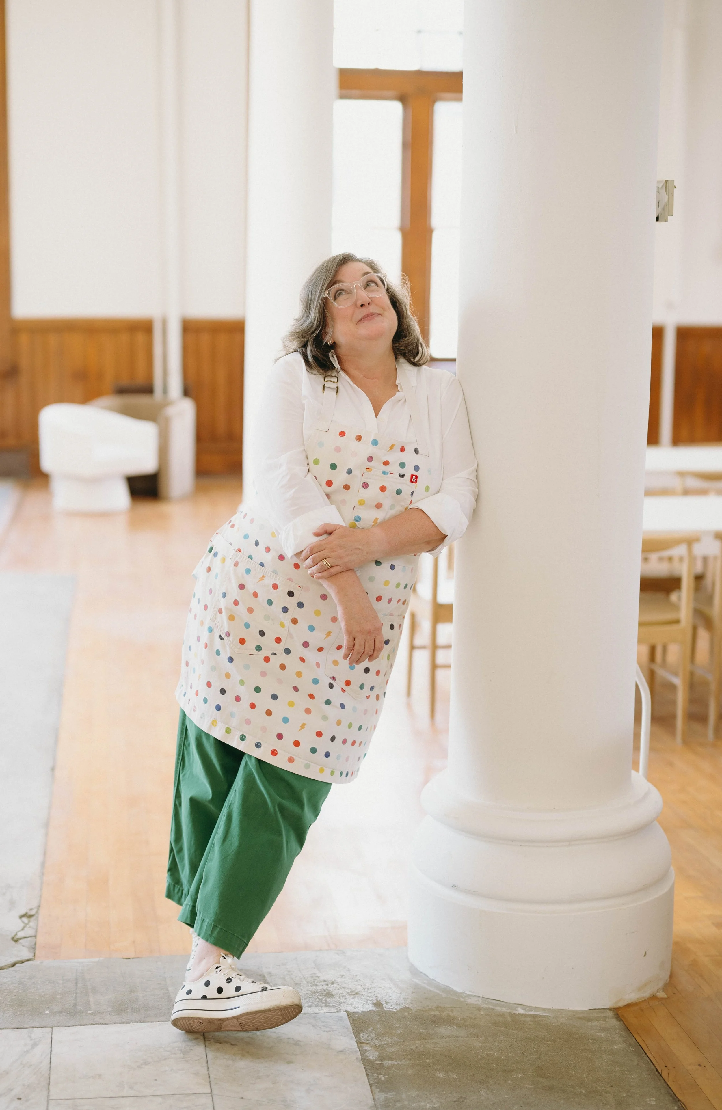 christine van bloem wearing a polka dot apron leaning against a post