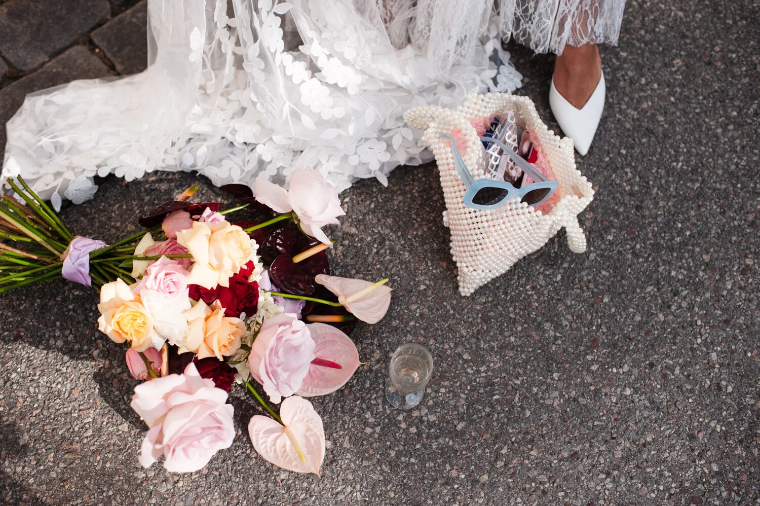Brudbukett, champagneglas, solglasögon och bröllopsklänning.