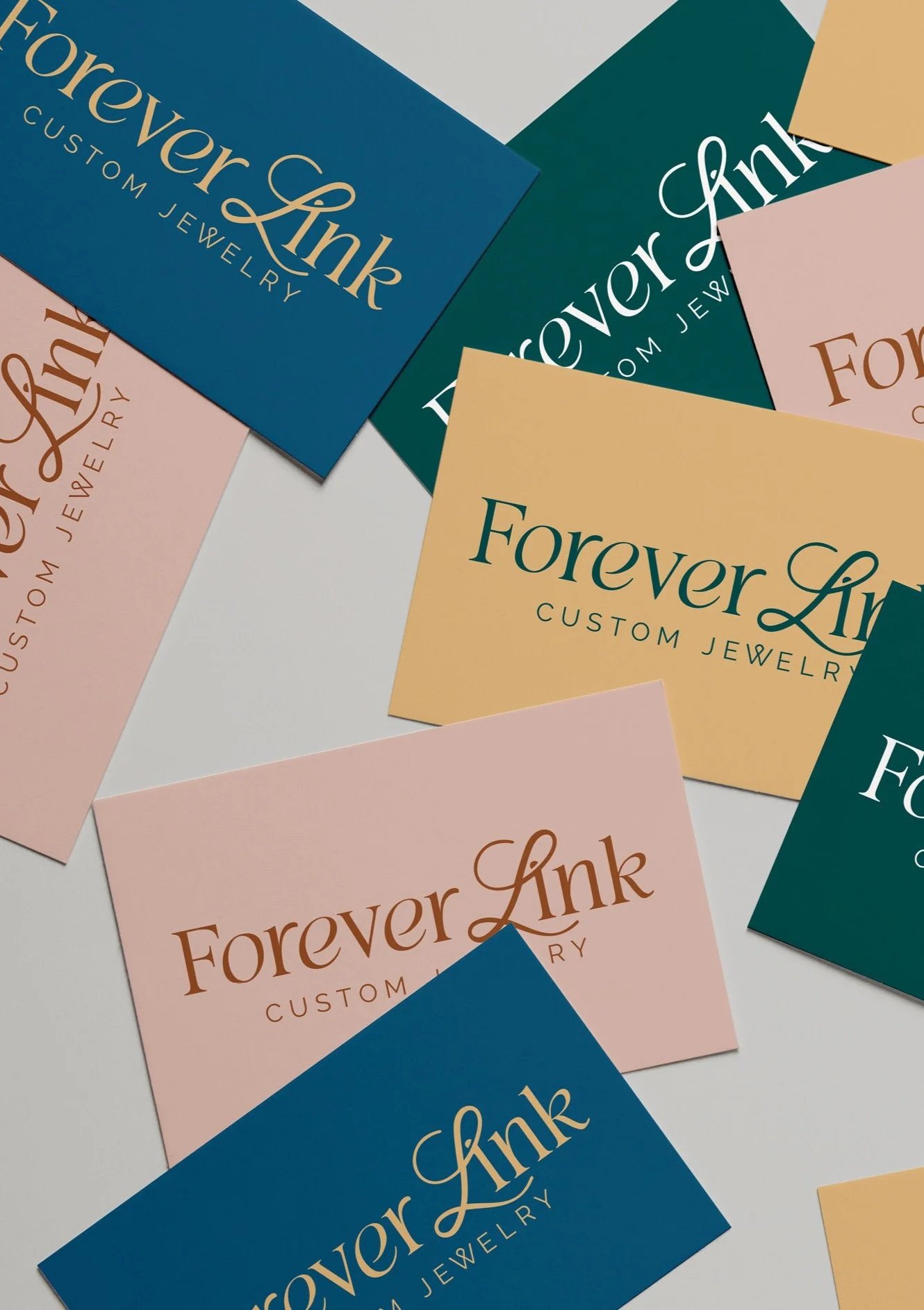 Business cards for Forever Link Custom Jewelry in various colors, scattered on a white surface.