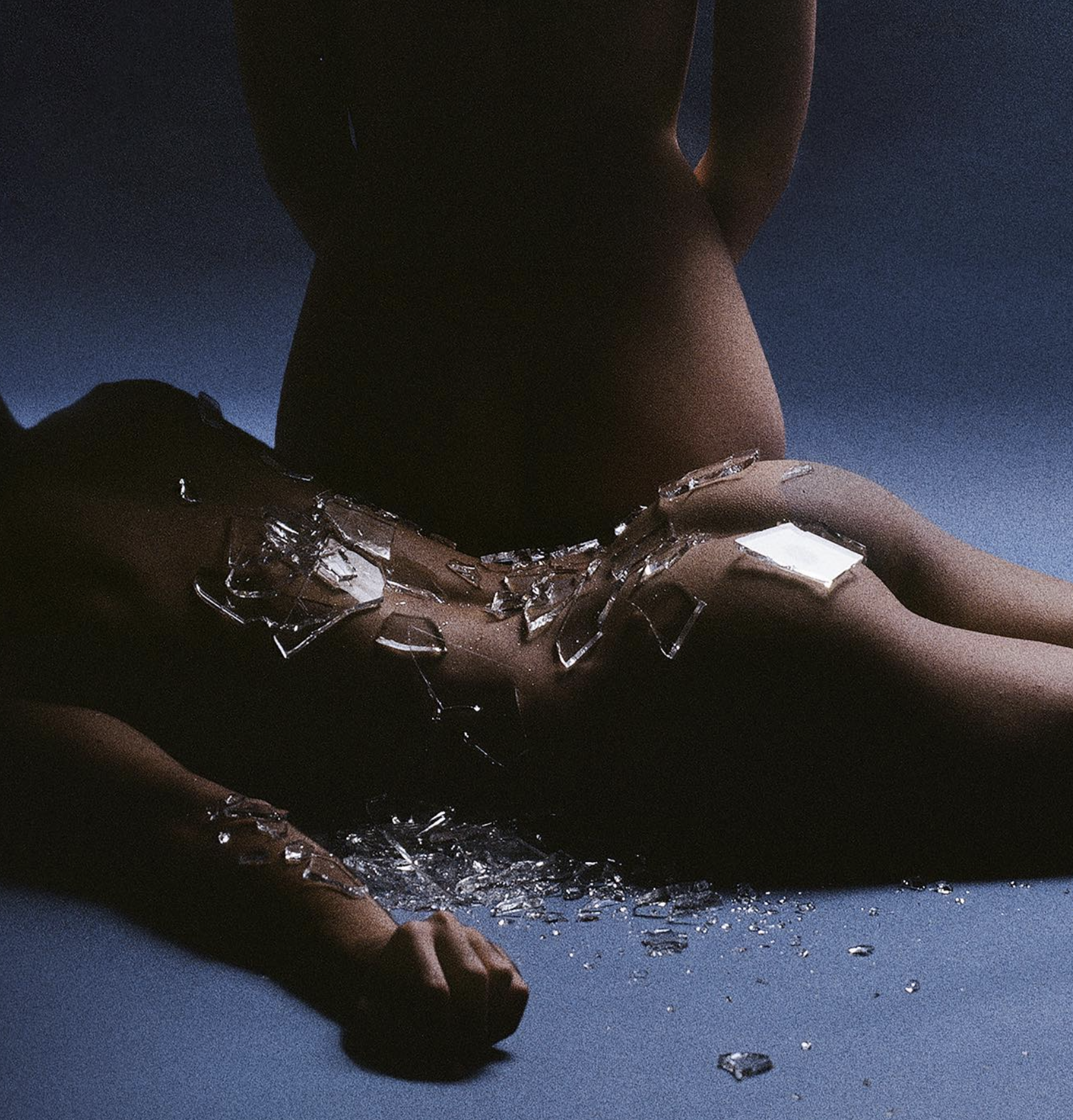 A person sitting on the floor with shattered glass around them, with their face not visible.