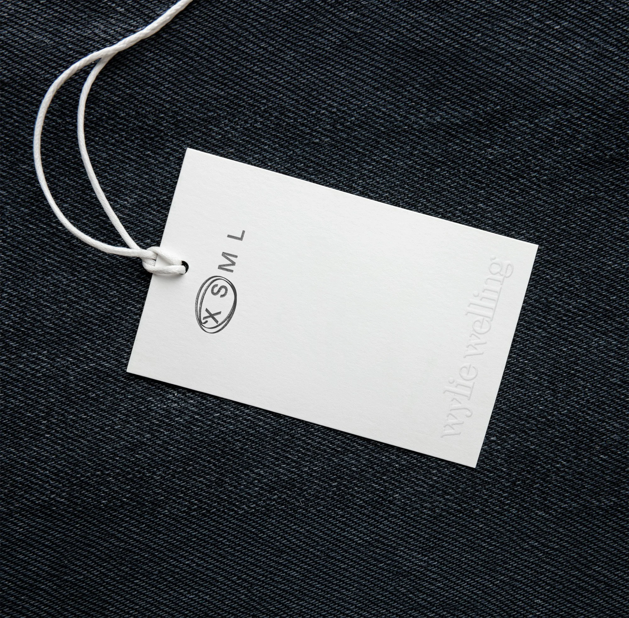 Minimalist hangtag design by Scorpion Rose Studio and Lafayette American on dark denim. Features an embossed wordmark and clean typography for premium apparel branding.