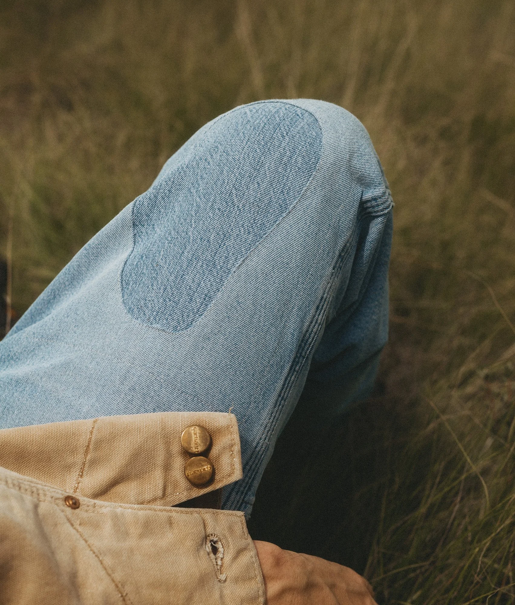 Close-up detail by Scorpion Rose Studio & Lafayette American: Vintage light-wash denim with a reinforced knee patch and tan canvas jacket cuff, highlighting tactile workwear textures.