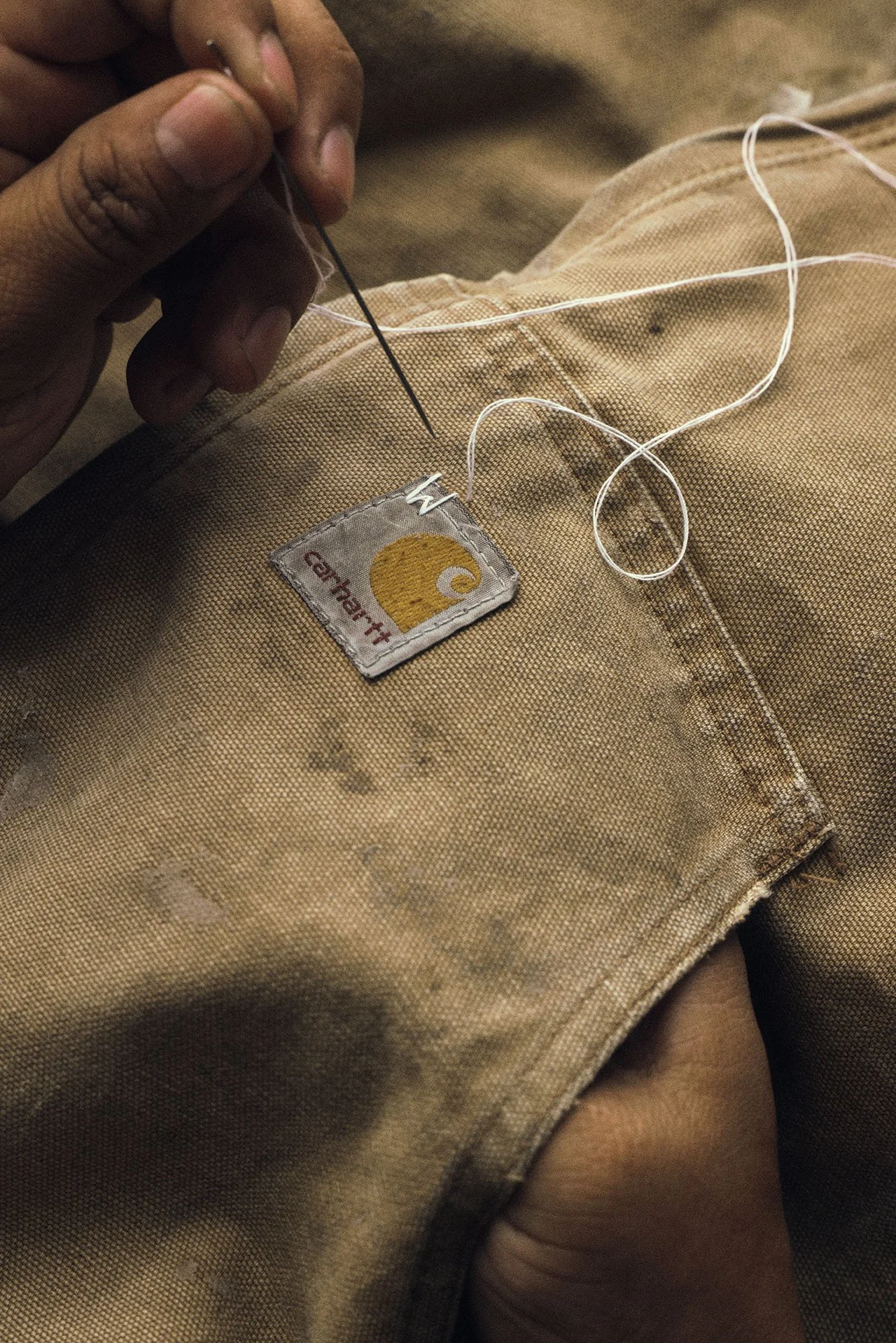 Close-up by Scorpion Rose Studio & Lafayette American: Artisan hand-stitching a custom "W" logo onto a vintage Carhartt label, showcasing bespoke branding and tactile craftsmanship.