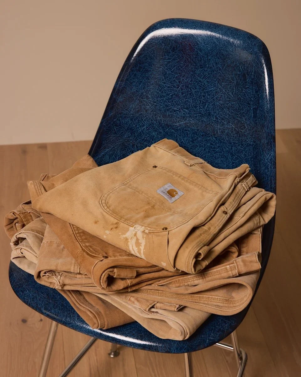 Stacked vintage Wylie Welling workwear on a blue Eames-style chair, curated by Scorpion Rose Studio and Lafayette American to showcase heritage apparel and brand art direction.