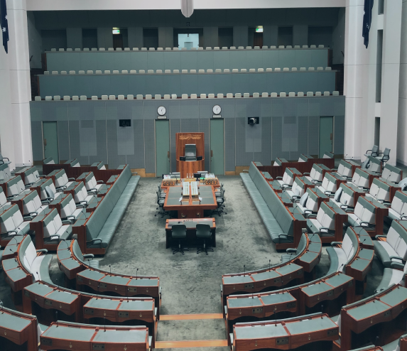 Empty legislative chamber with semi-circular rows of seats and a central desk at the front.