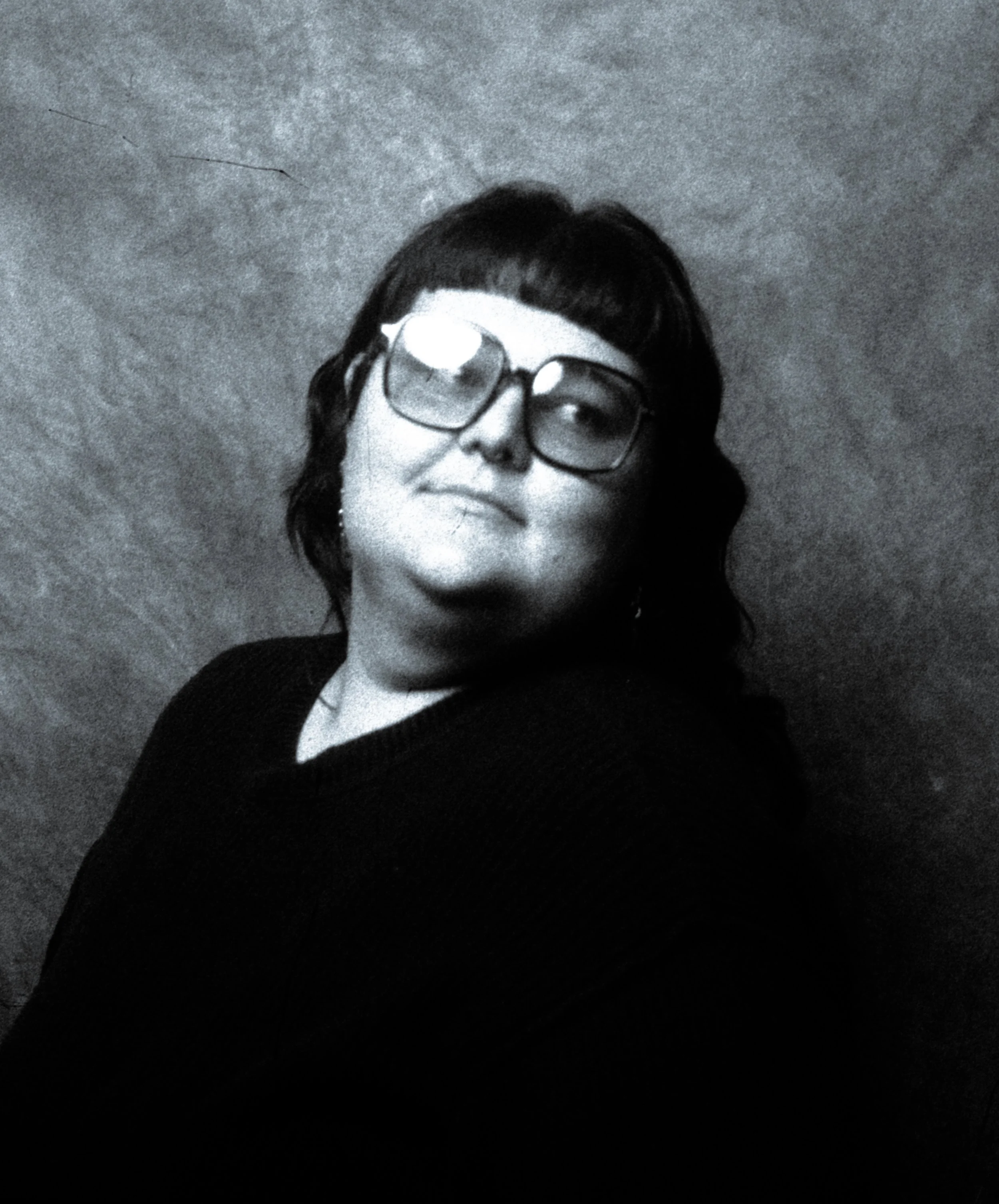 A person with short dark hair and glasses, looking slightly upward and to the side, against a plain textured background.