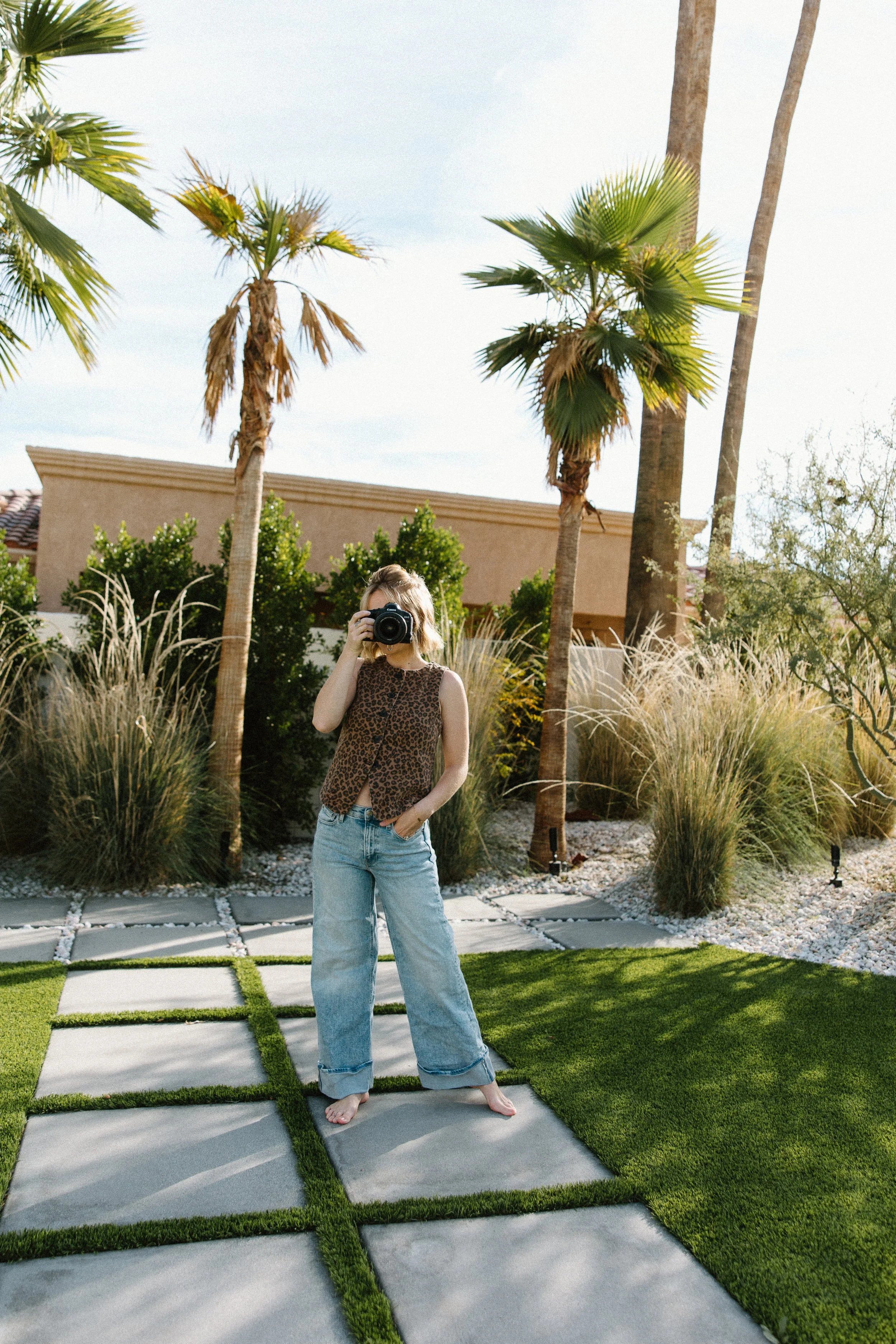 Person taking a photo with a camera in a backyard with palm trees and grass.