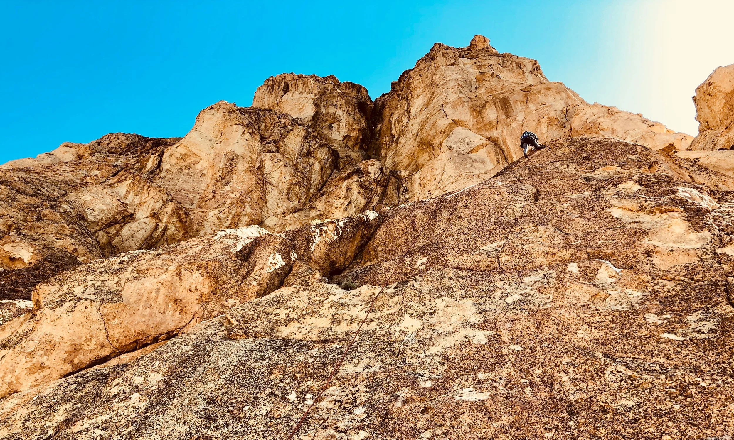 Climber ascending a rocky cliff face with a blue sky in the background.