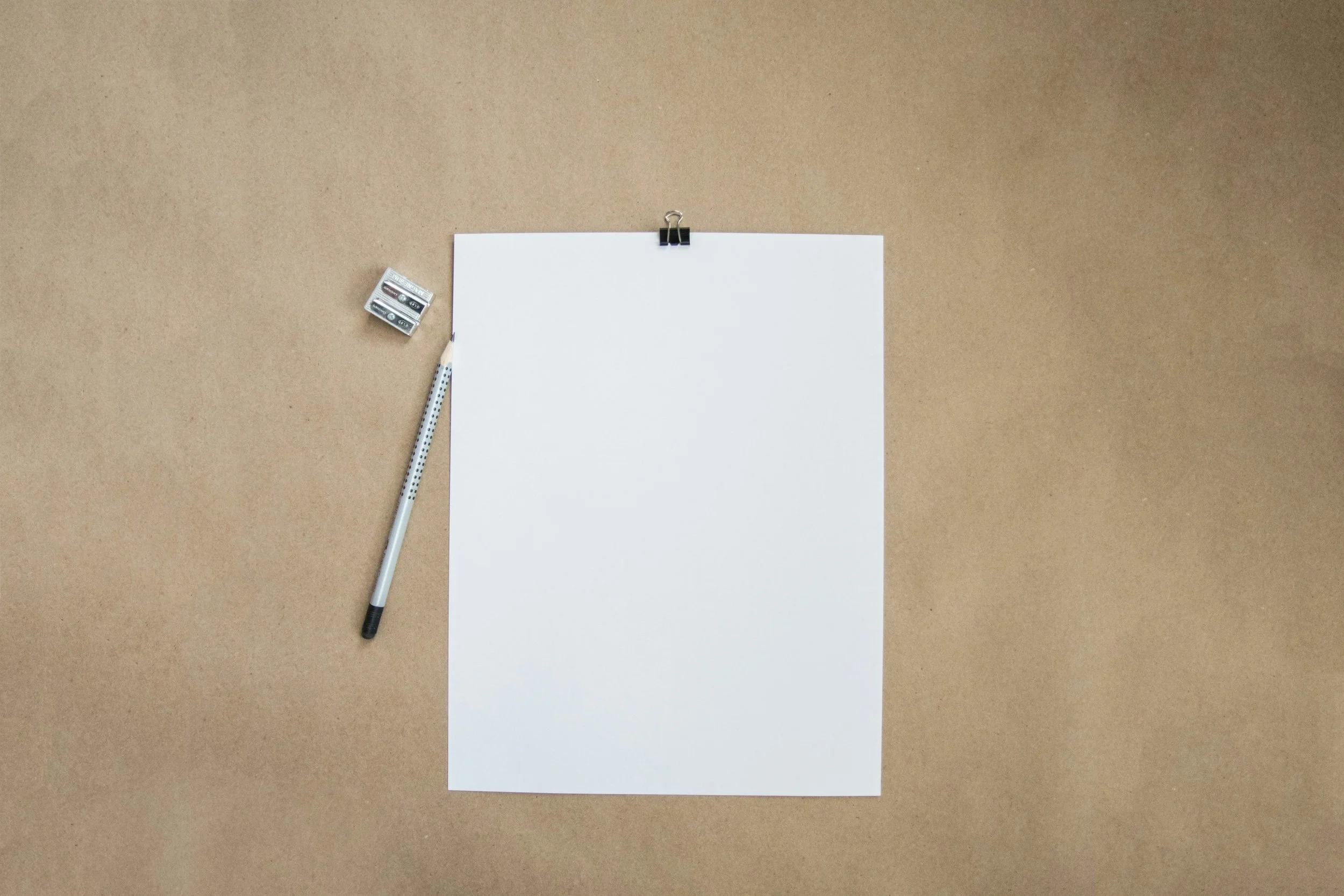 Blank white sheet of paper clipped to a corkboard, with a pencil and battery nearby.
