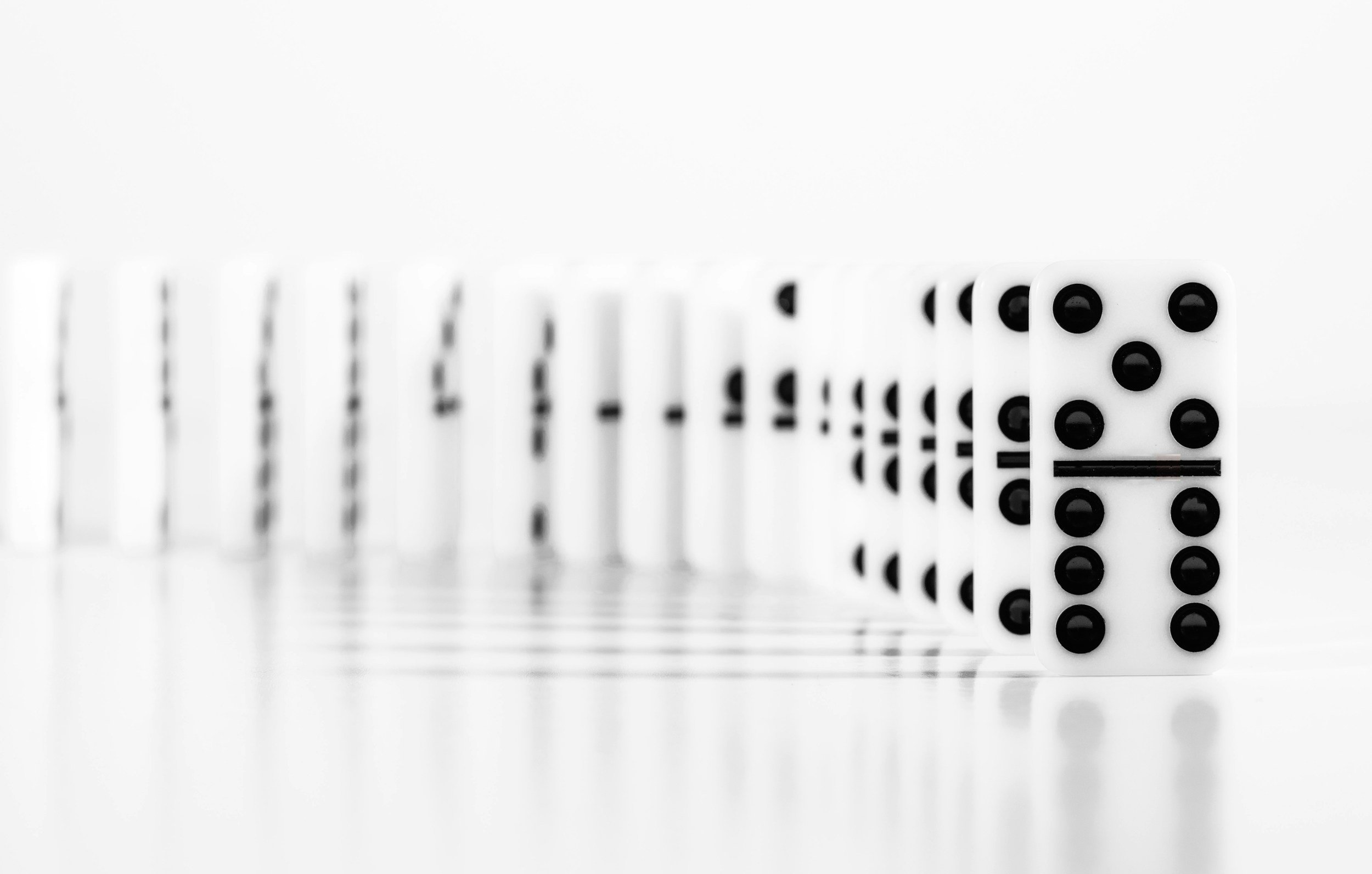 Close-up of domino tiles standing in a line on a reflective surface with a white background.