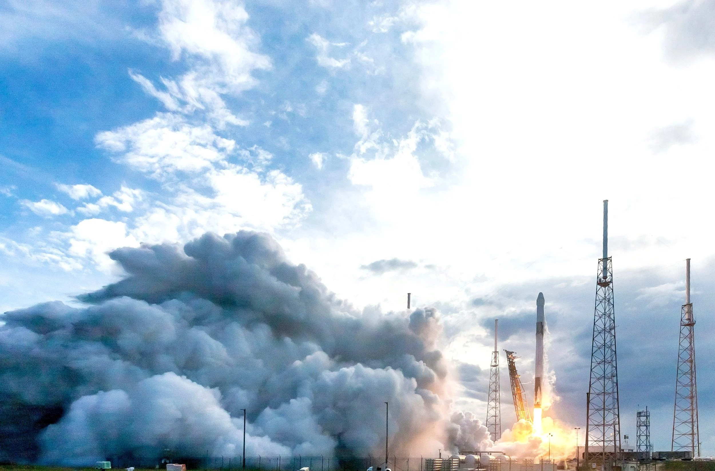 Rocket launch with plume of smoke and towers, blue sky background.