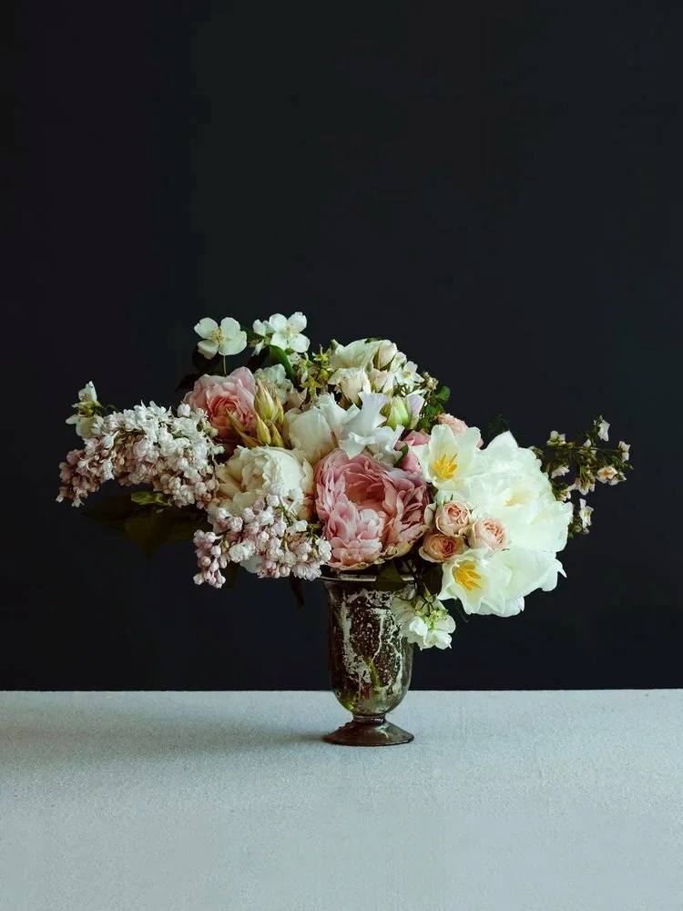 A bouquet of pink and white flowers in a decorative vase on a white table, with a dark gray background.