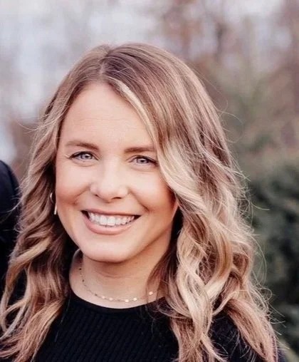 Headshot of a young woman with light brown, wavy hair smiling outdoors