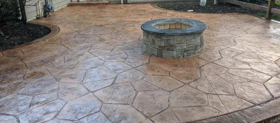 A flagstone stamped patio with dark border surrounds a stone firepit
