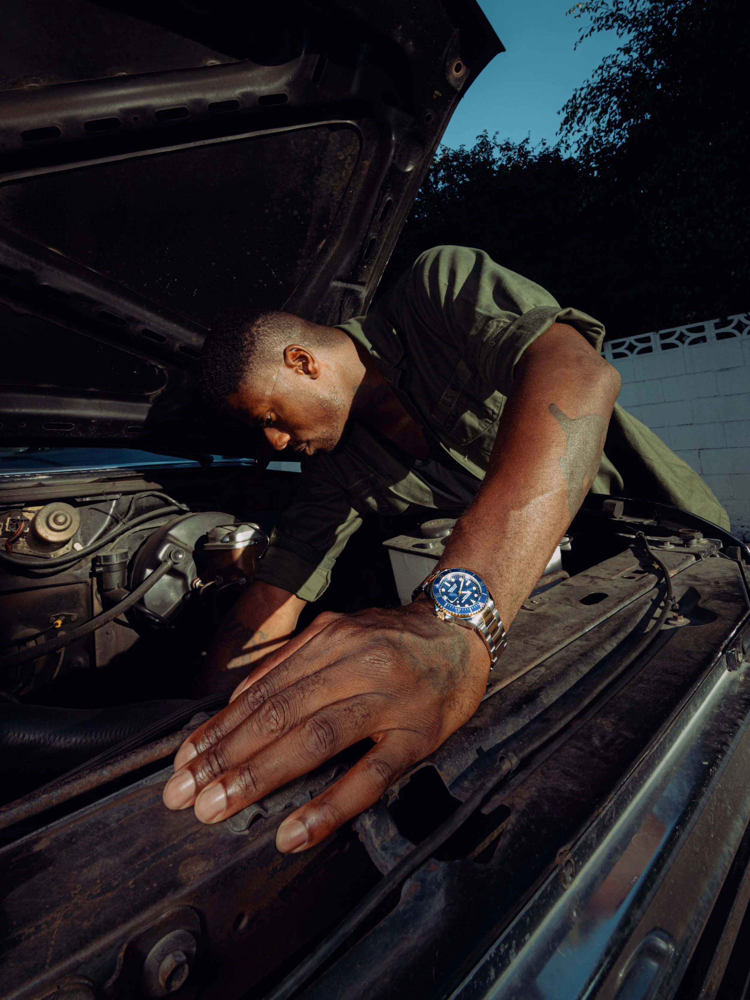 A man looking under the hood of a car, working on the engine during the daytime.