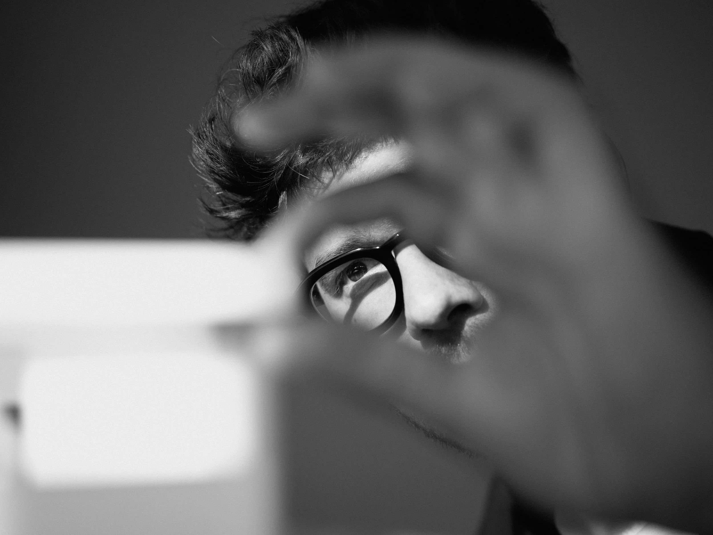 A person with glasses looking at a computer screen, seen through their hand.