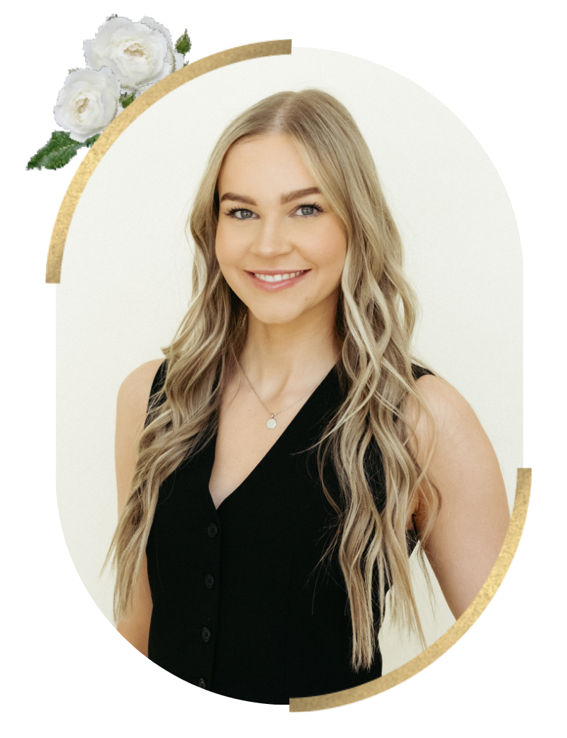A smiling woman with long blonde wavy hair, wearing a black sleeveless top and a necklace, standing against a white background. There are white roses and gold accents in the image design.