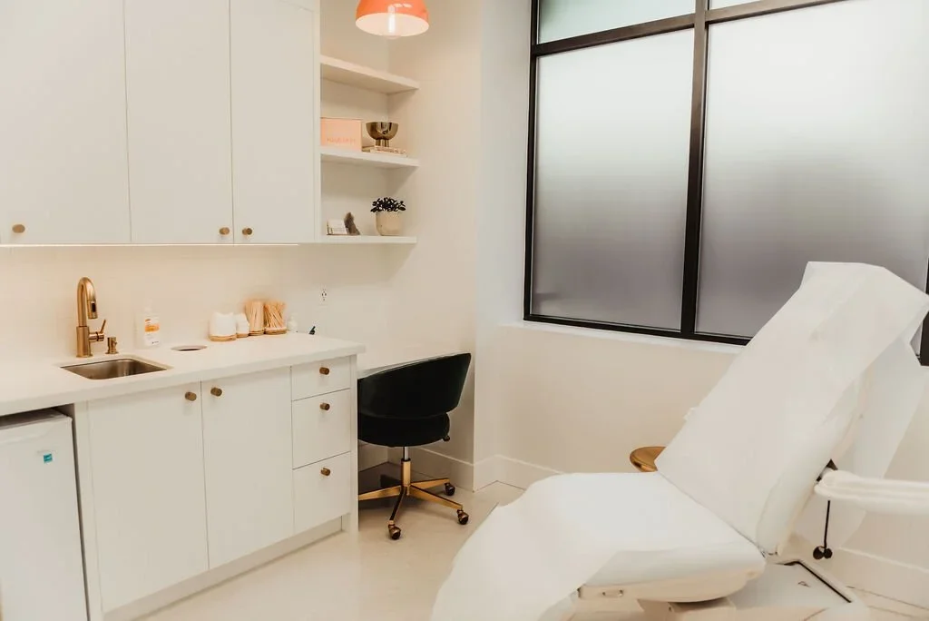Medical examination room with white cabinetry, a black chair, a patient bed, and frosted window