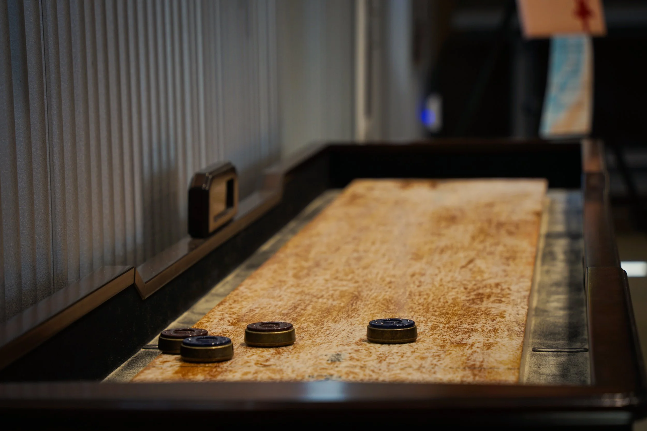 Shuffleboard table with four pucks and a wall-mounted scorekeeper in a game room.