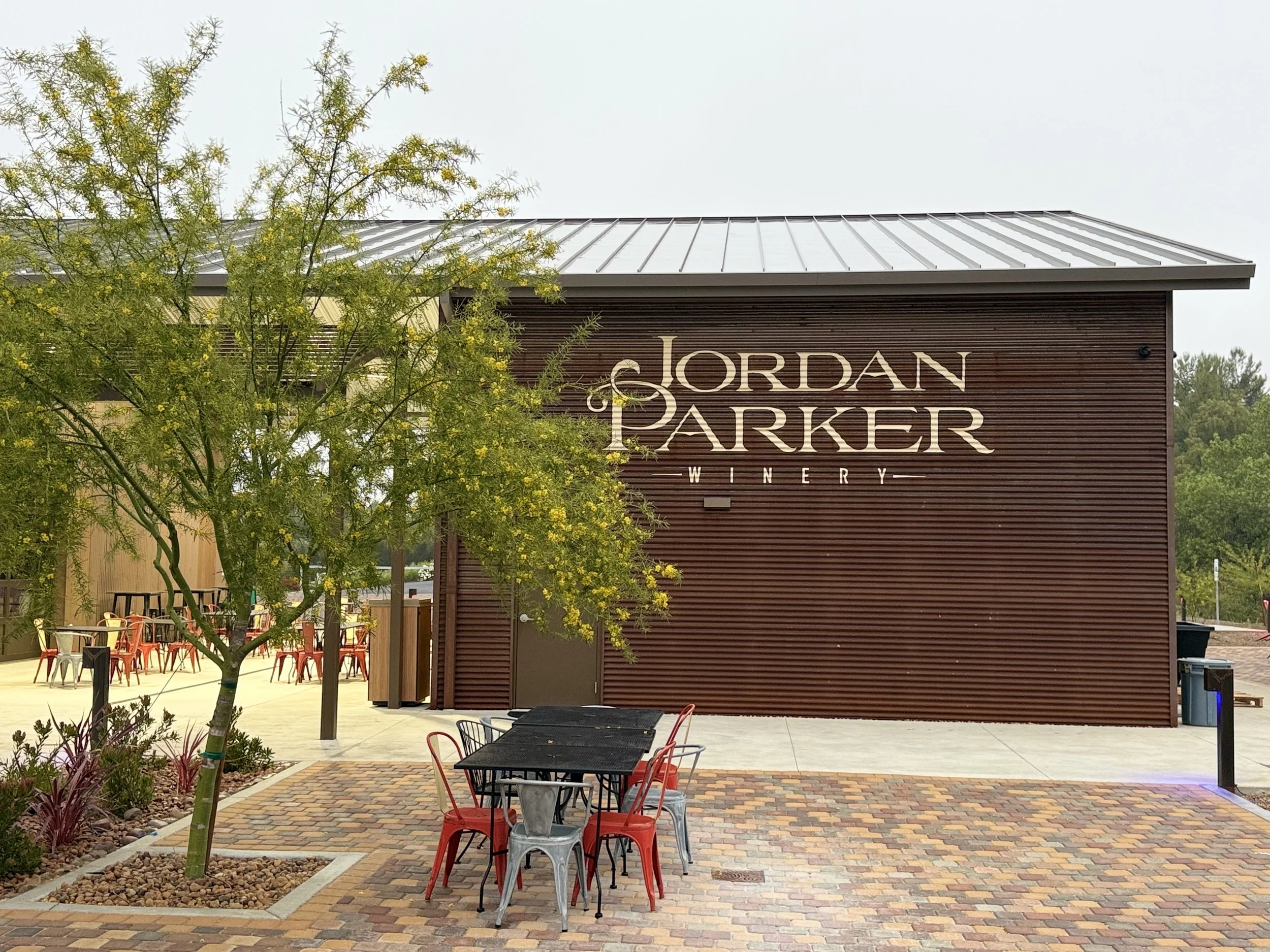 Exterior view of Jordan & Parker Winery with outdoor seating, brick pathway, trees, and a modern wooden building.