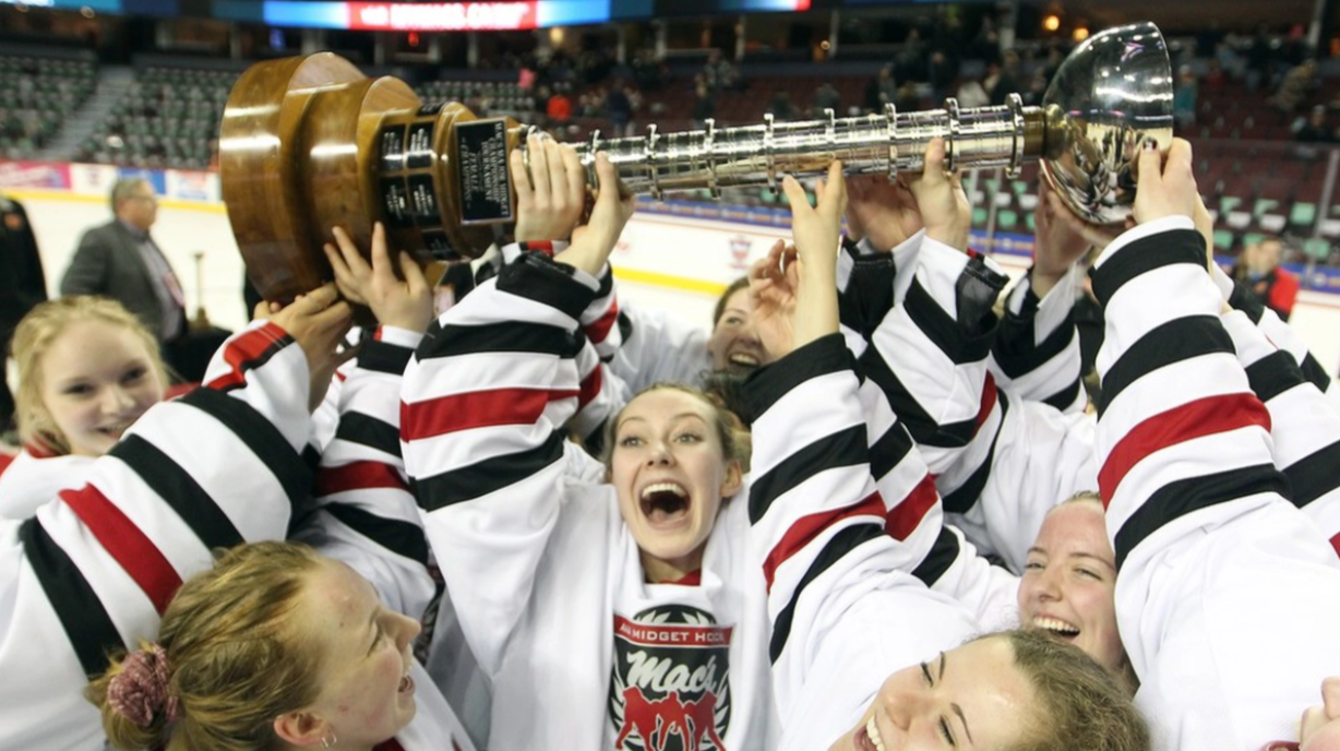 Hockey players celebrating with a large trophy after winning a game in an ice rink.