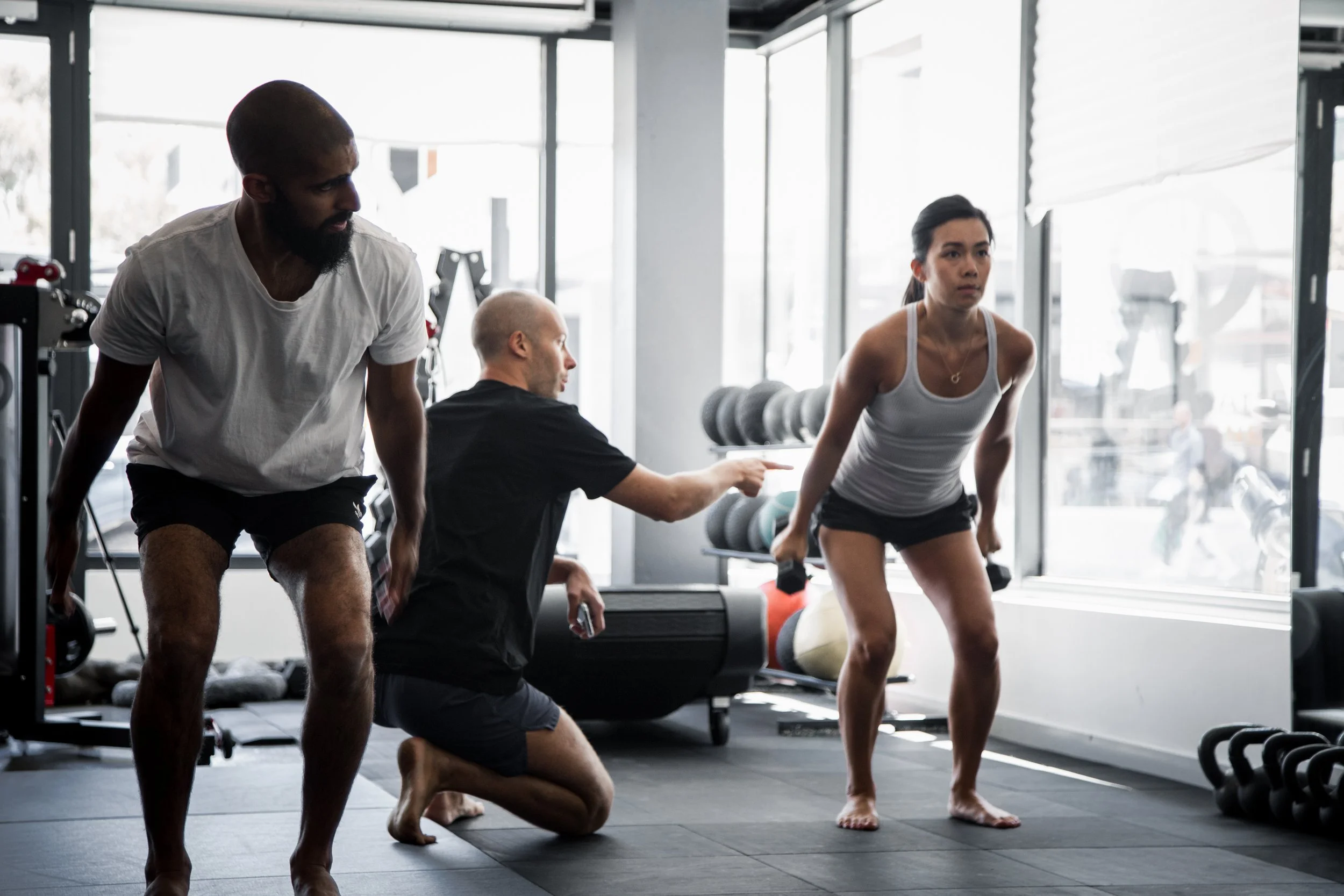 A Functional Patterns melbourne client doing a kettlebell exercise under the supervision of a trainer in the gym.
