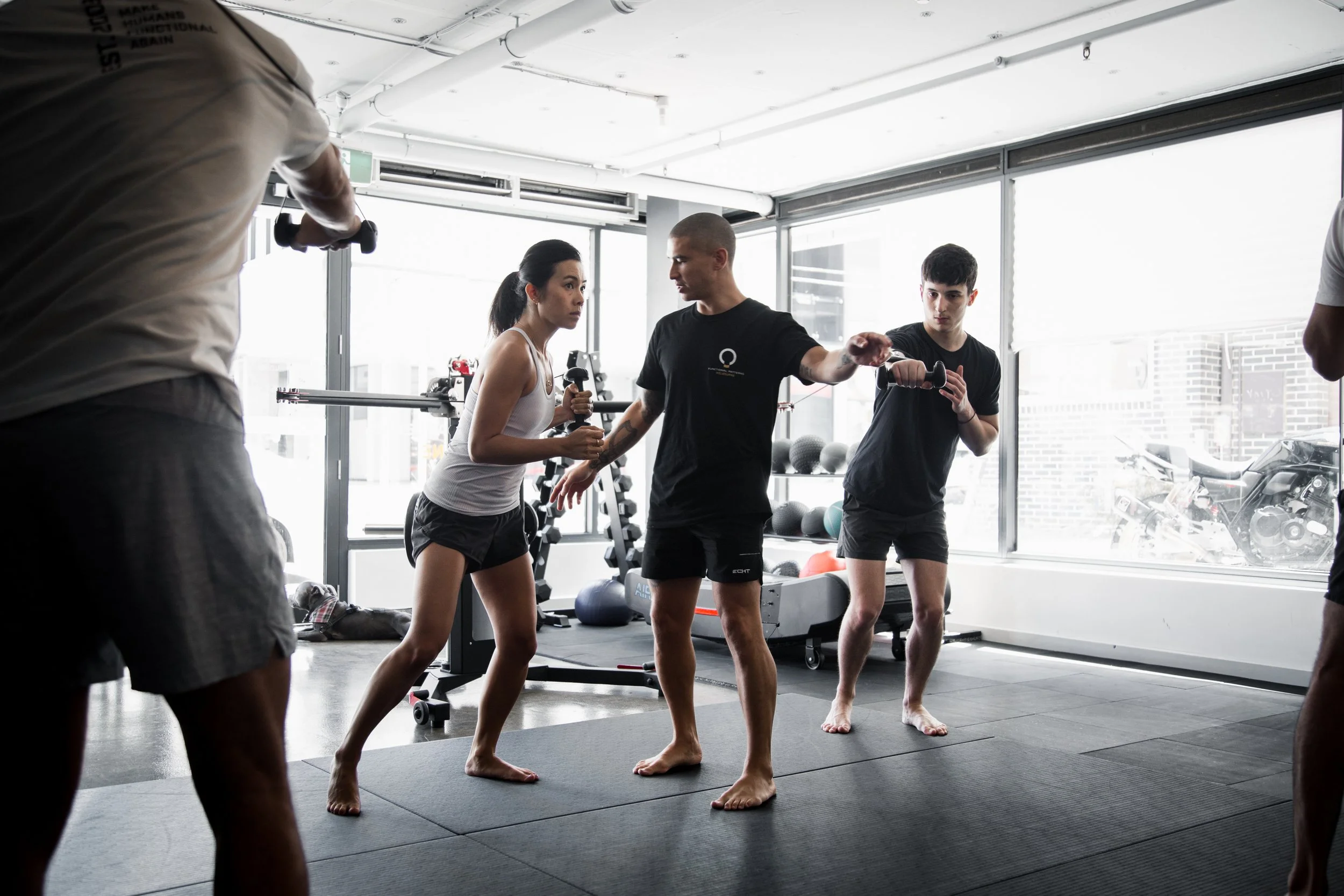 A fitness instructor demonstrating boxing techniques to a female and two male clients in a gym.