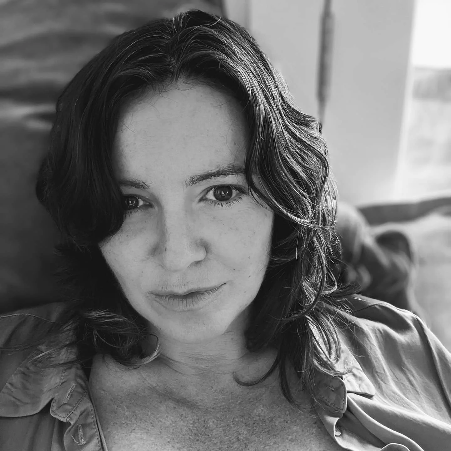 Black and white portrait of a person with medium-length hair, wearing a button-up shirt, looking directly at the camera.