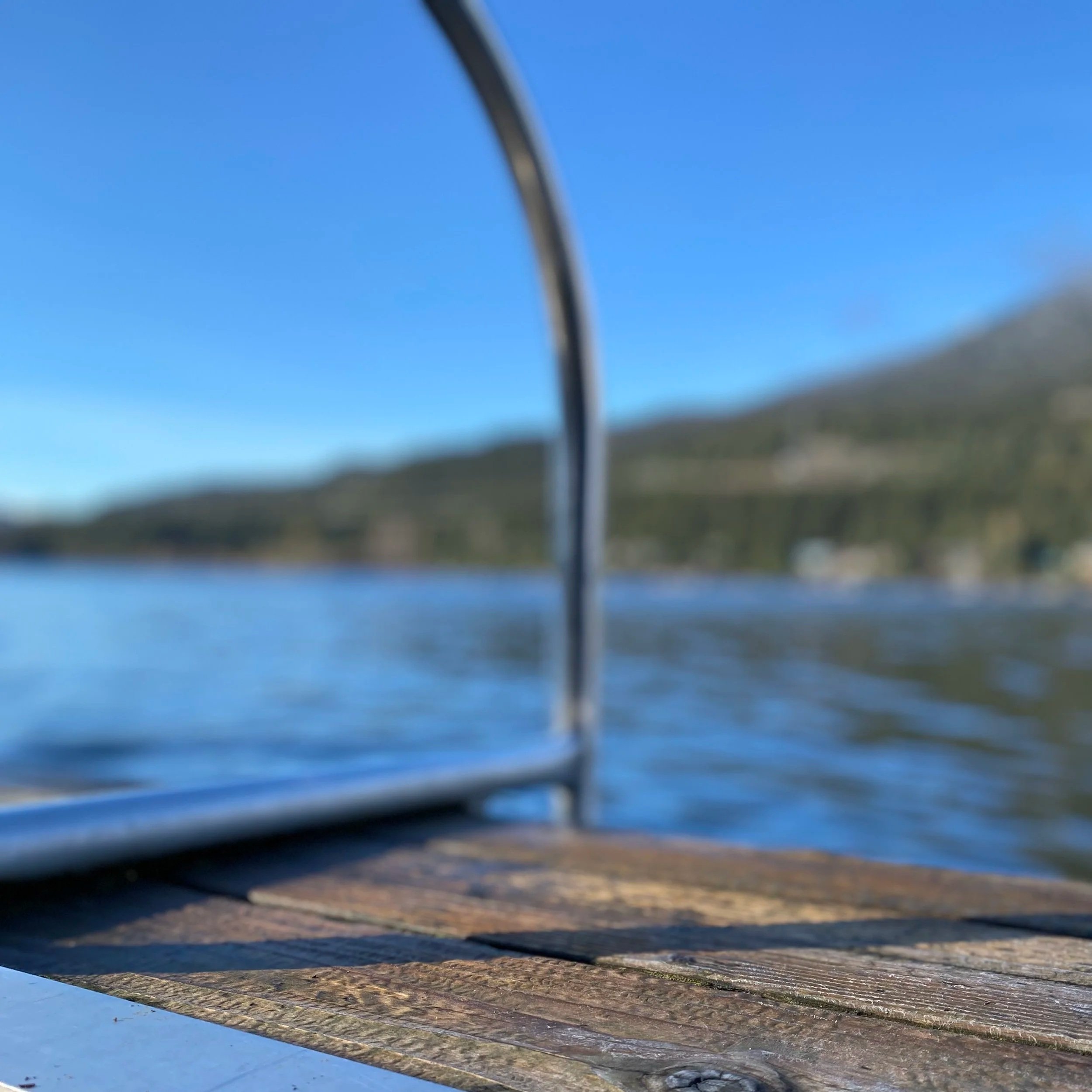 Alta Lake, Whistler BC. Close-up of a metal handle on a wooden dock with water, mountains, and clear blue sky in the background.