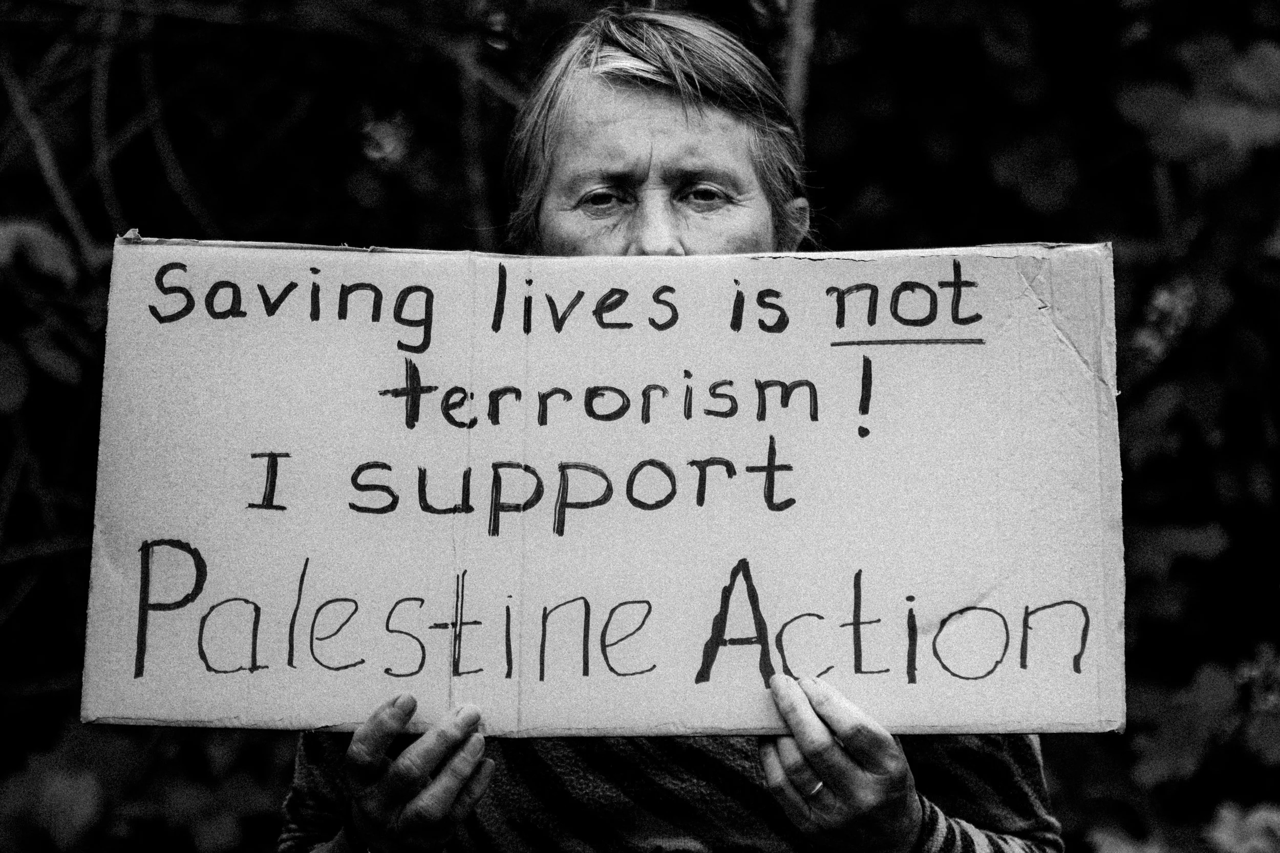 Woman holding a sign reading 'Saving lives is not terrorism! I support Palestine Action' outside Woolwich Crown Court