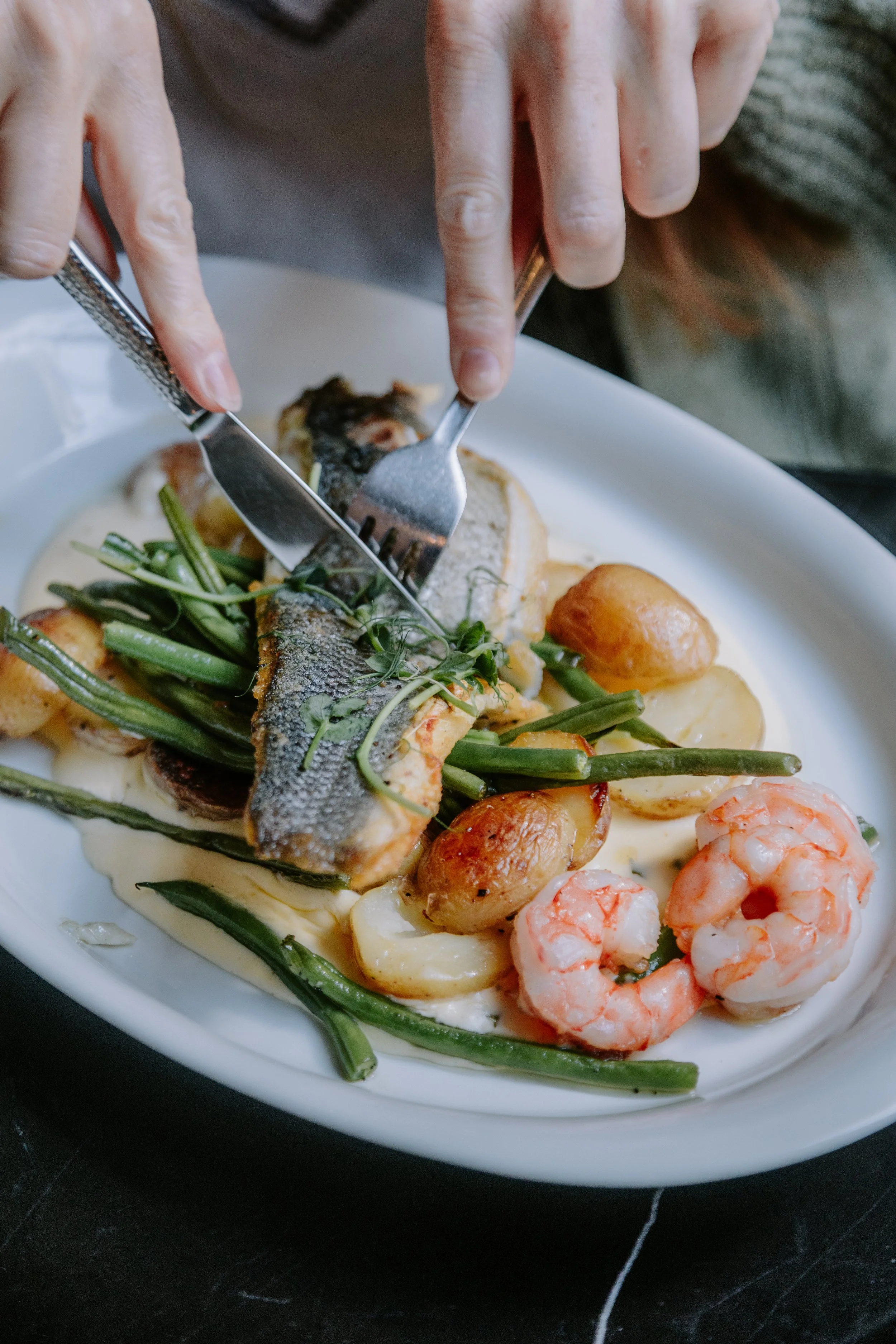 A seafood dish with cooked shrimp, fish, potatoes, green beans, and garnished herbs on a white plate. york leeds yorkshire restaurant photographer videographer