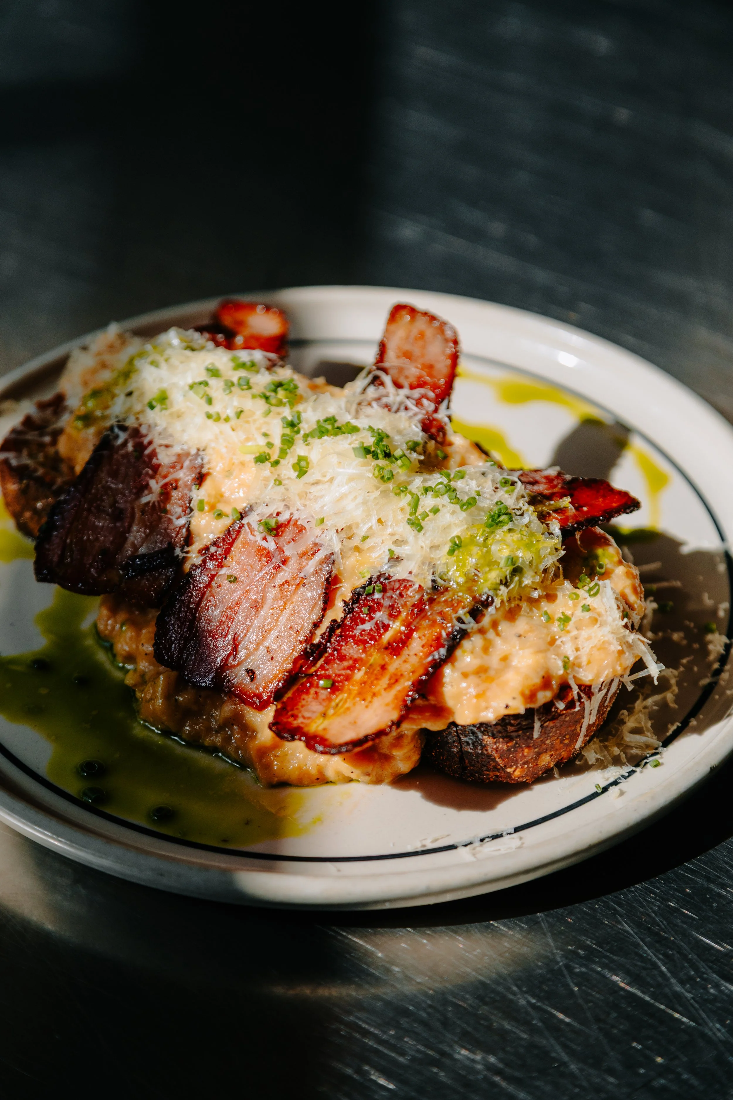 Close-up of a gourmet dish with grilled meat, topped with grated cheese, chopped herbs, and a roasted tomato on a white plate with olive oil drizzle. york leeds yorkshire restaurant photographer videographer